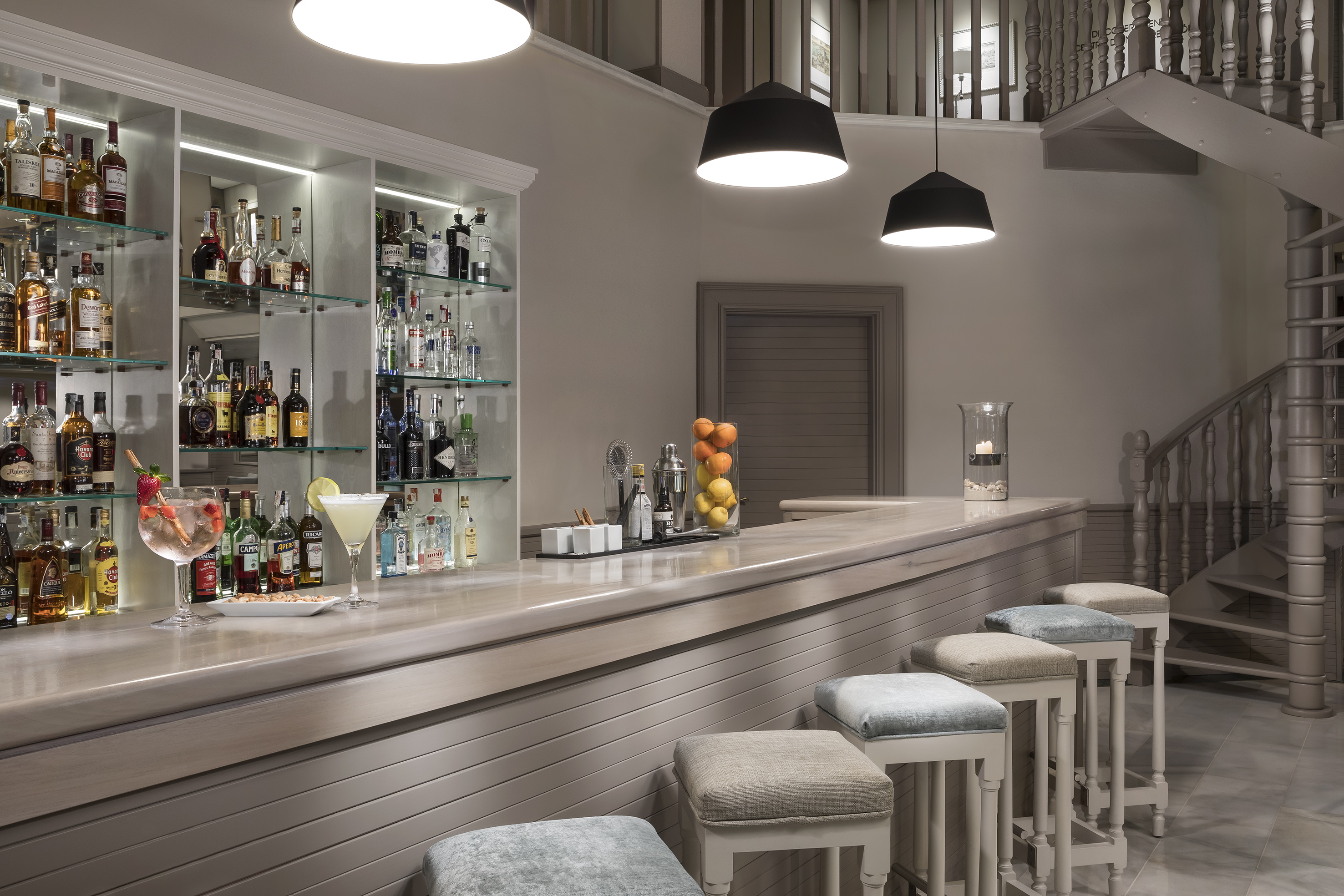 Modern bar counter with liquor bottles, cocktails, bar stools, spiral staircase.