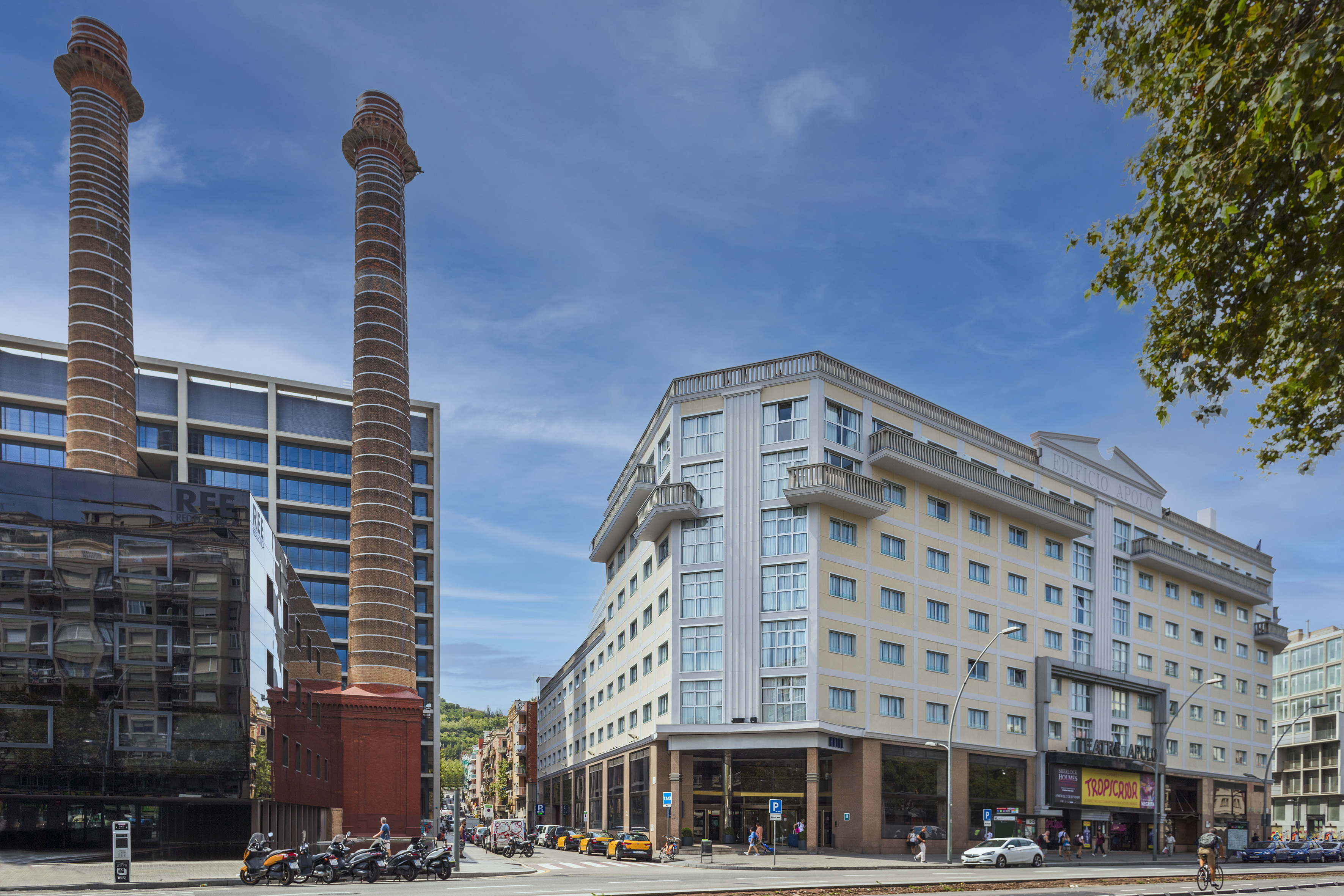 Barcelona street scene with twin brick chimneys, modern offices, and Edificio Apolo.