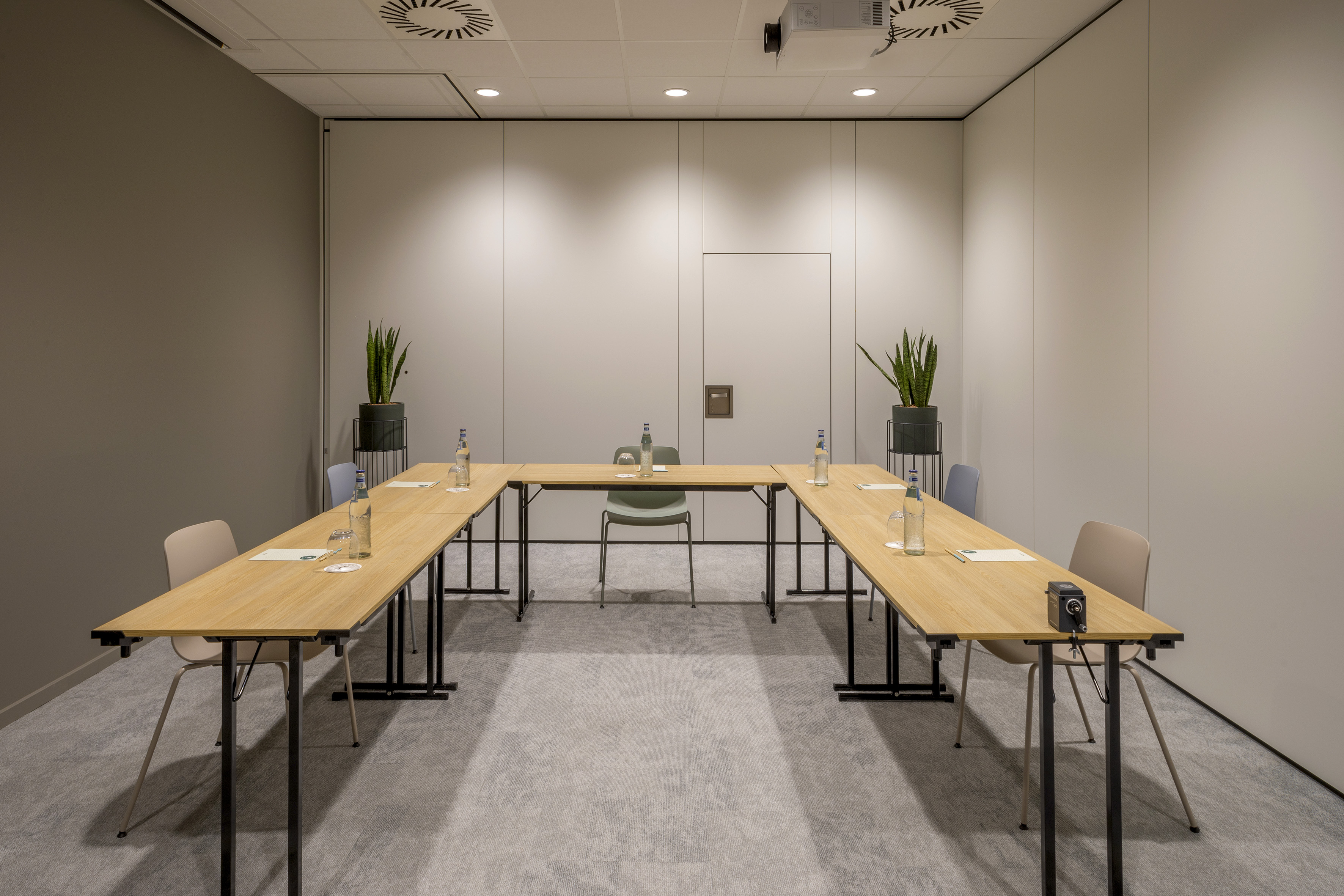 Modern conference room with U-shaped wooden tables, chairs, and projector.