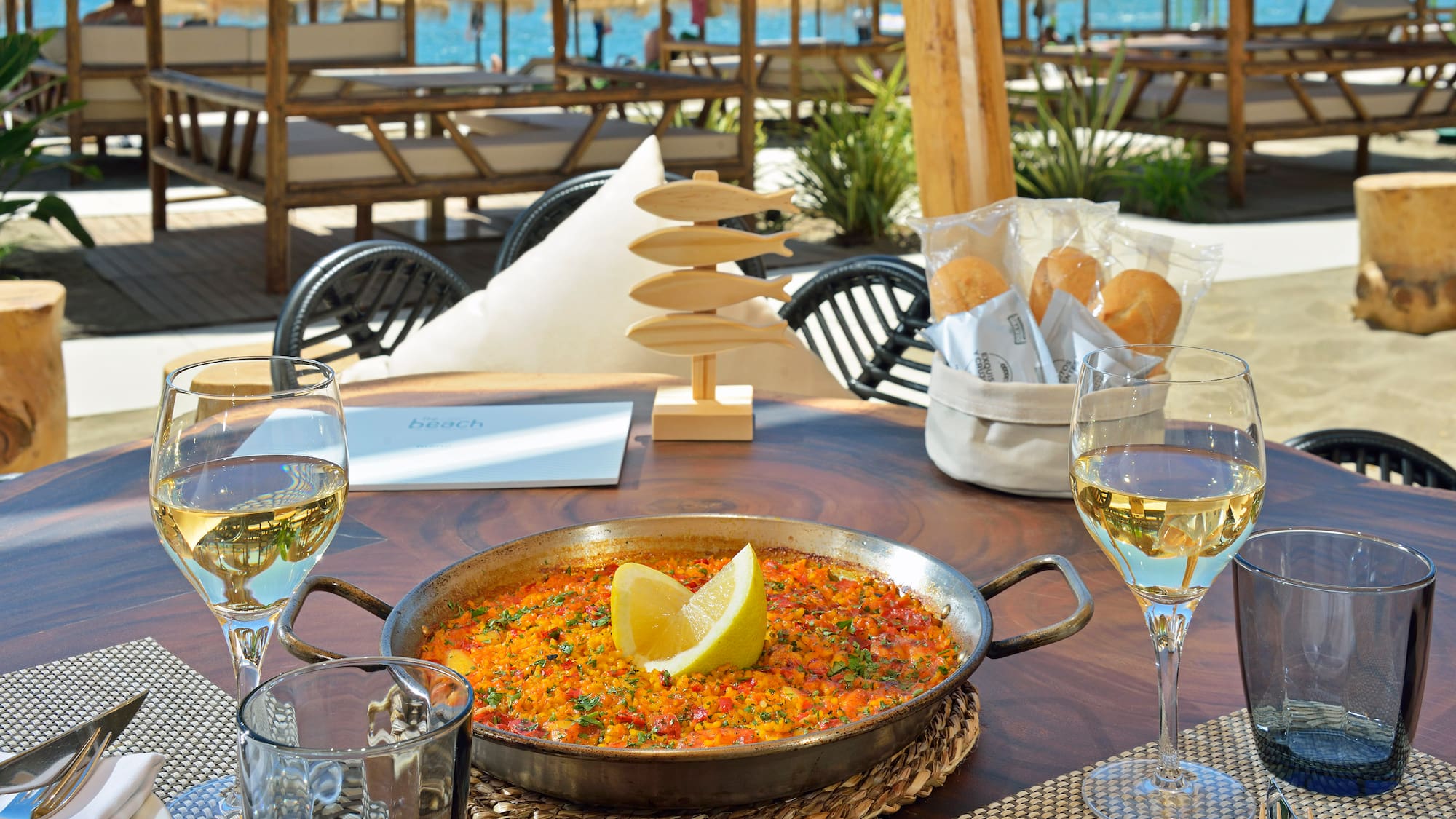 a pan of food on a table with wine glasses and a beach