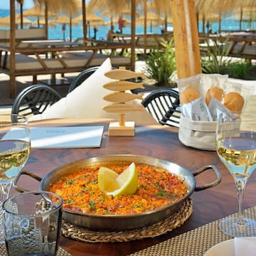 a pan of food on a table with wine glasses and a beach