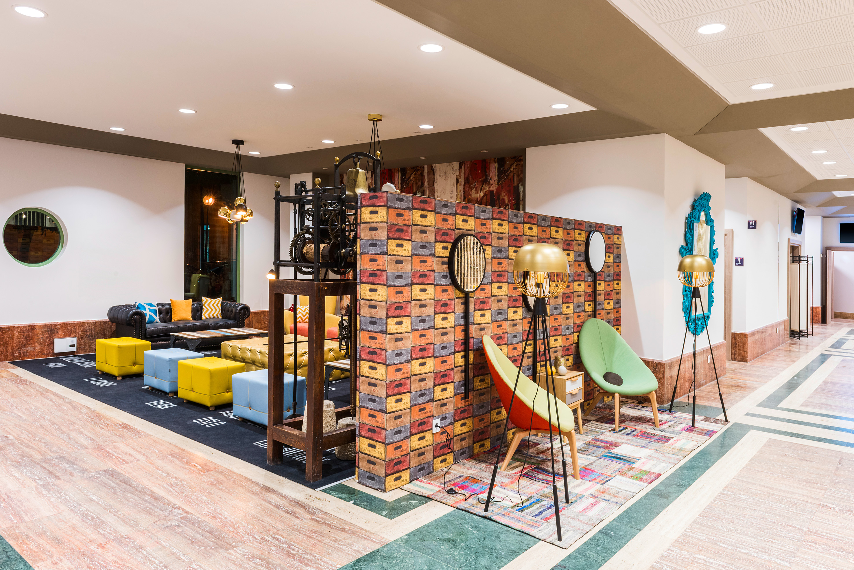 Eclectic hotel lounge with colorful furniture, patterned wall, and modern lighting.