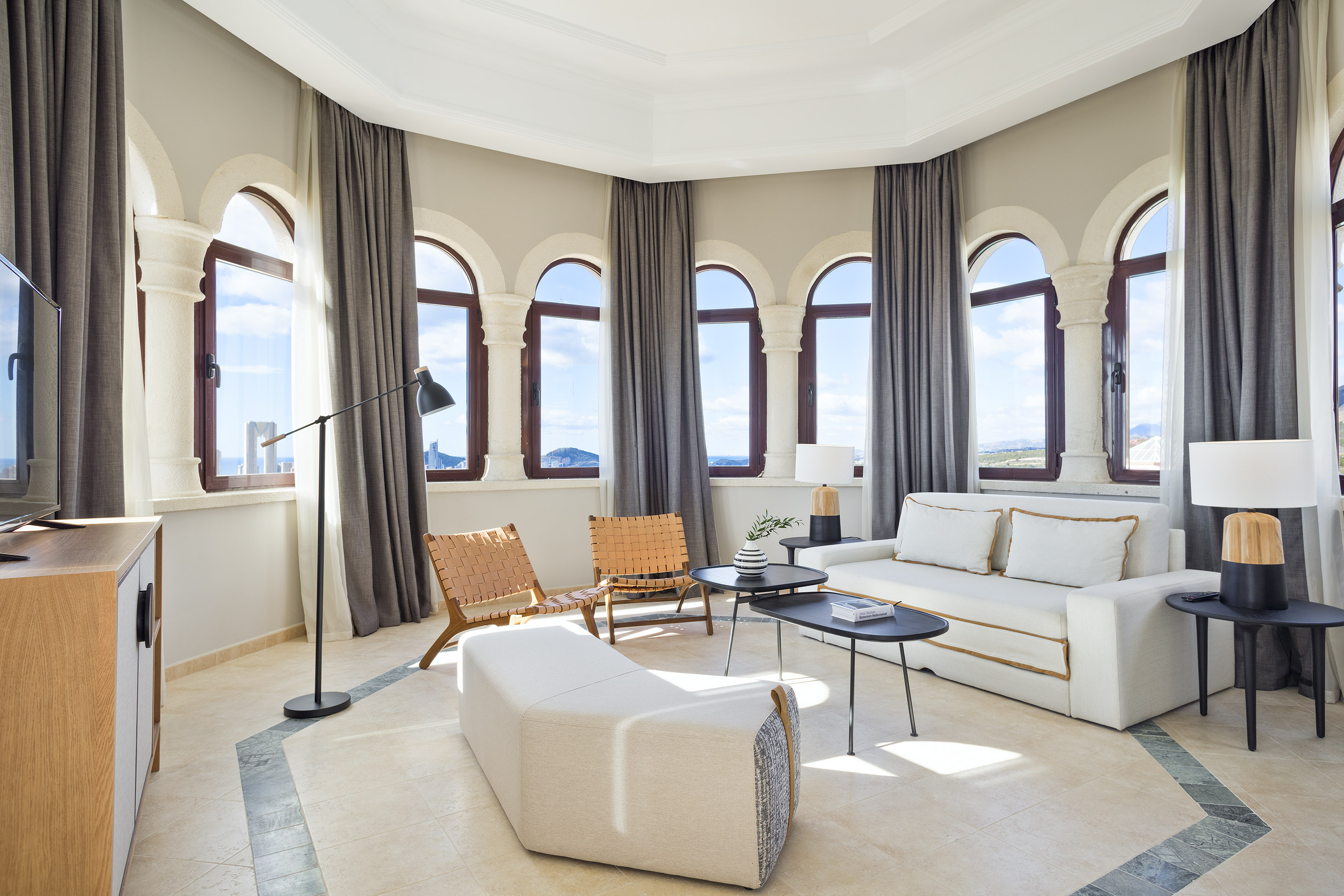 Hotel suite living room with arched windows, white sofa, and ocean view.