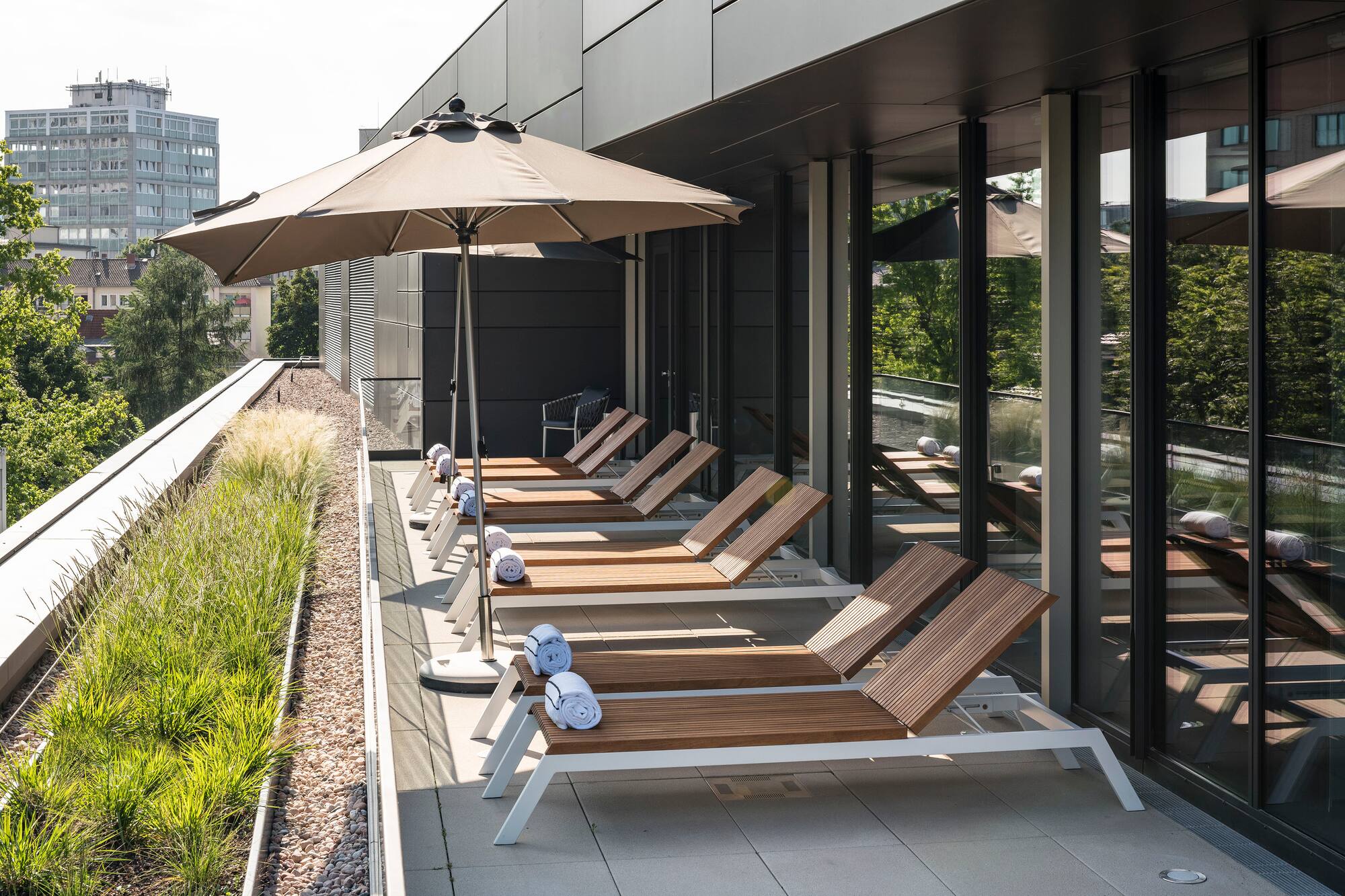 Modern rooftop terrace with sun loungers, umbrella, and green roof planters.