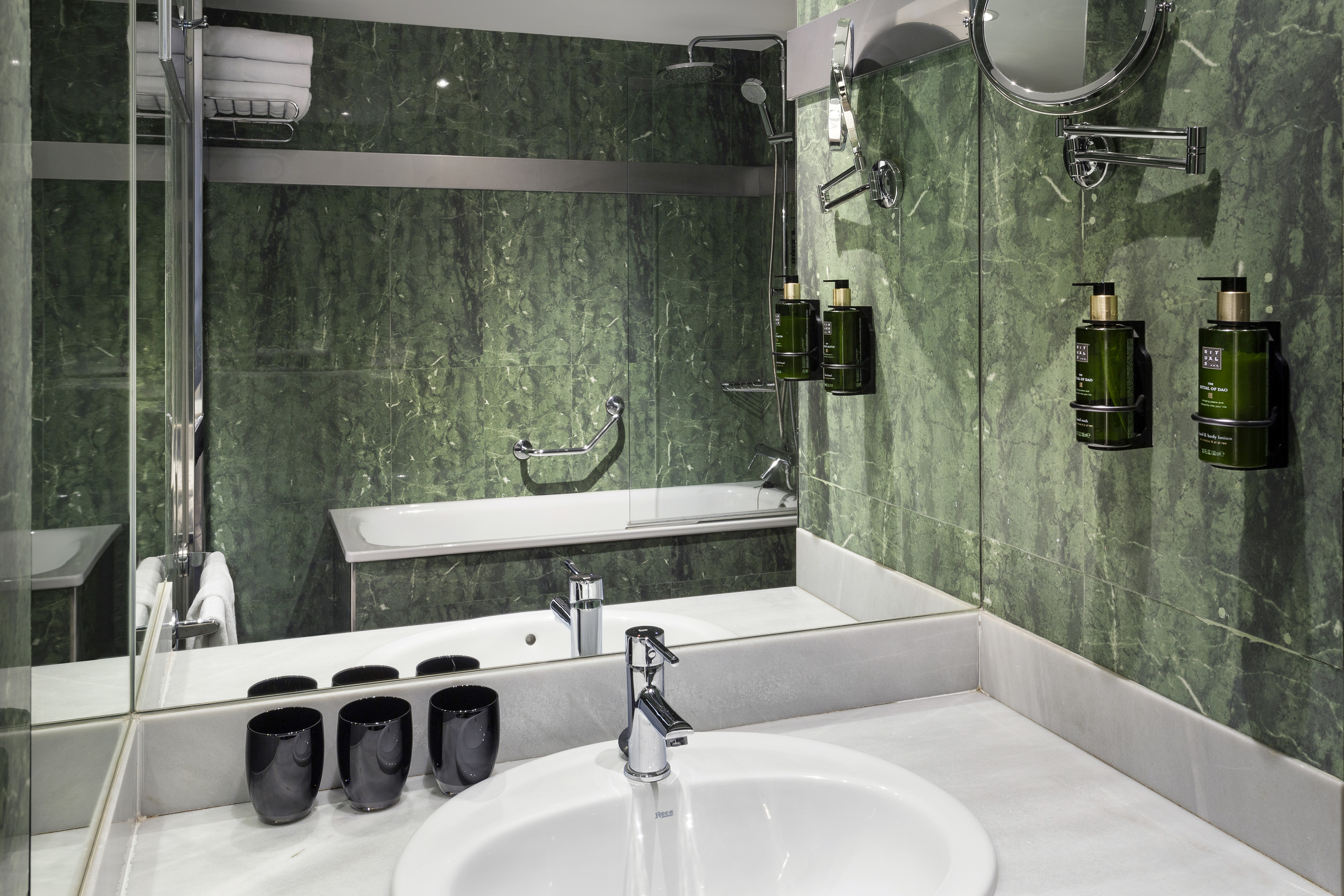 Modern hotel bathroom with green marble walls, sink, shower, and bathtub.