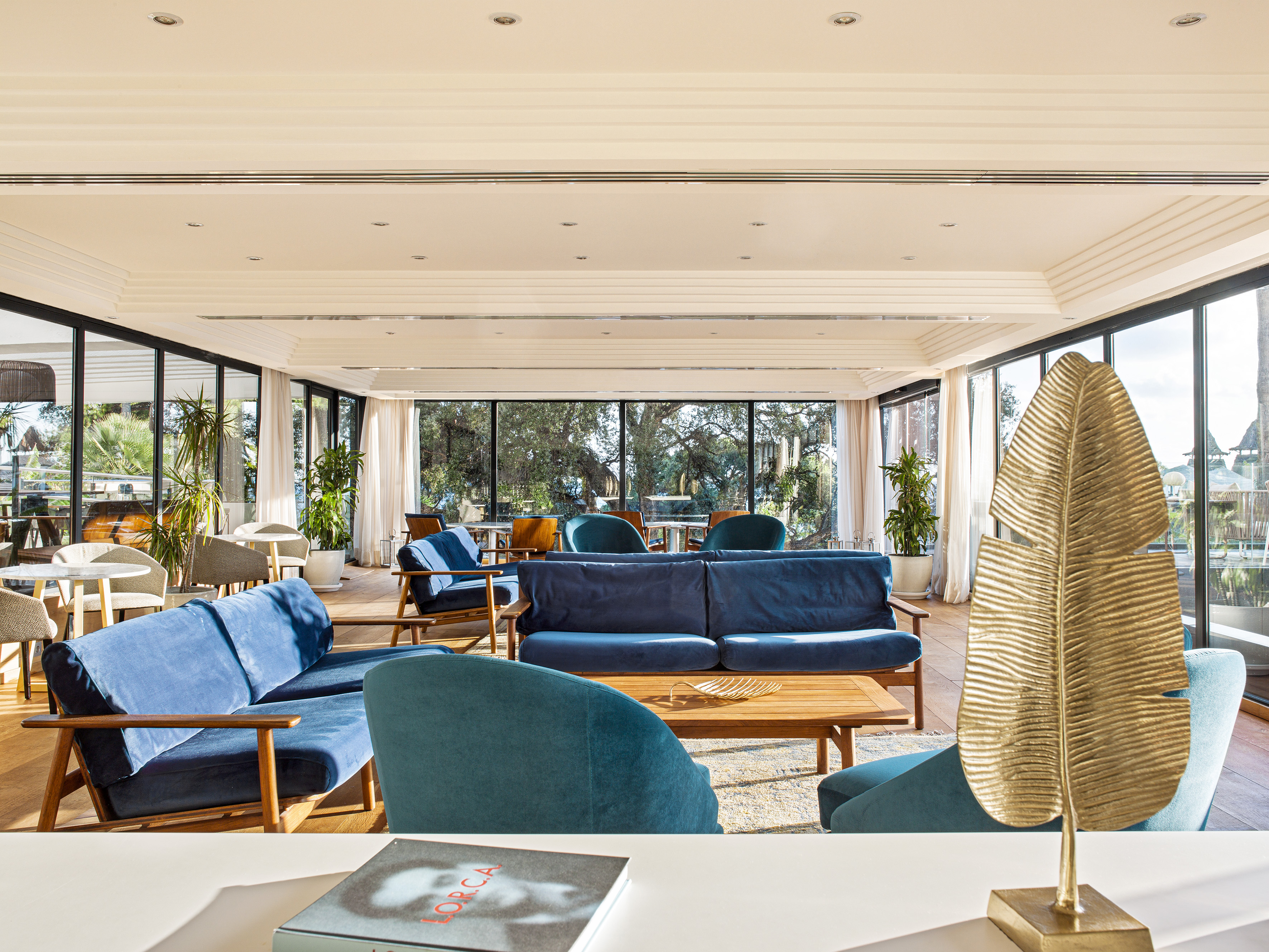 Modern hotel lounge with blue velvet sofas, large windows, and natural views.