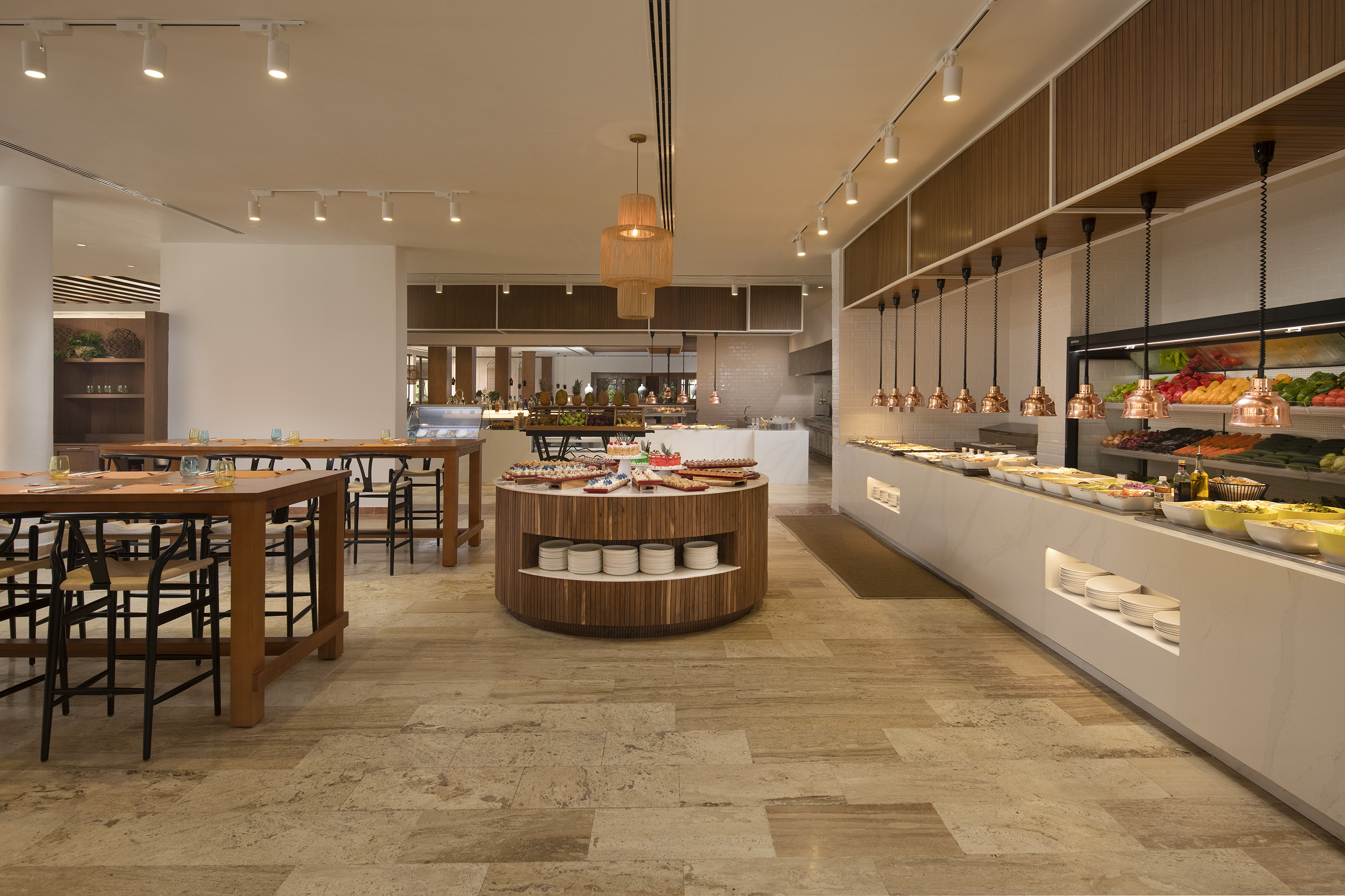 Hotel restaurant buffet with fresh food displays, desserts, and dining tables.