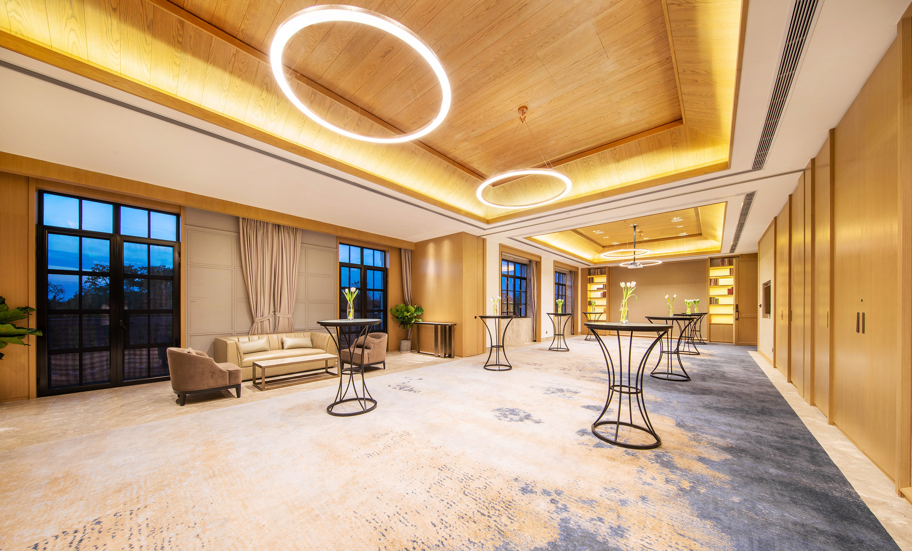 Elegant modern event room with wooden ceiling, circular lights, and cocktail tables.