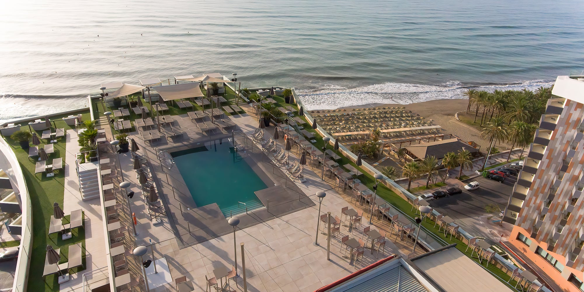 a pool and chairs on a rooftop overlooking a beach