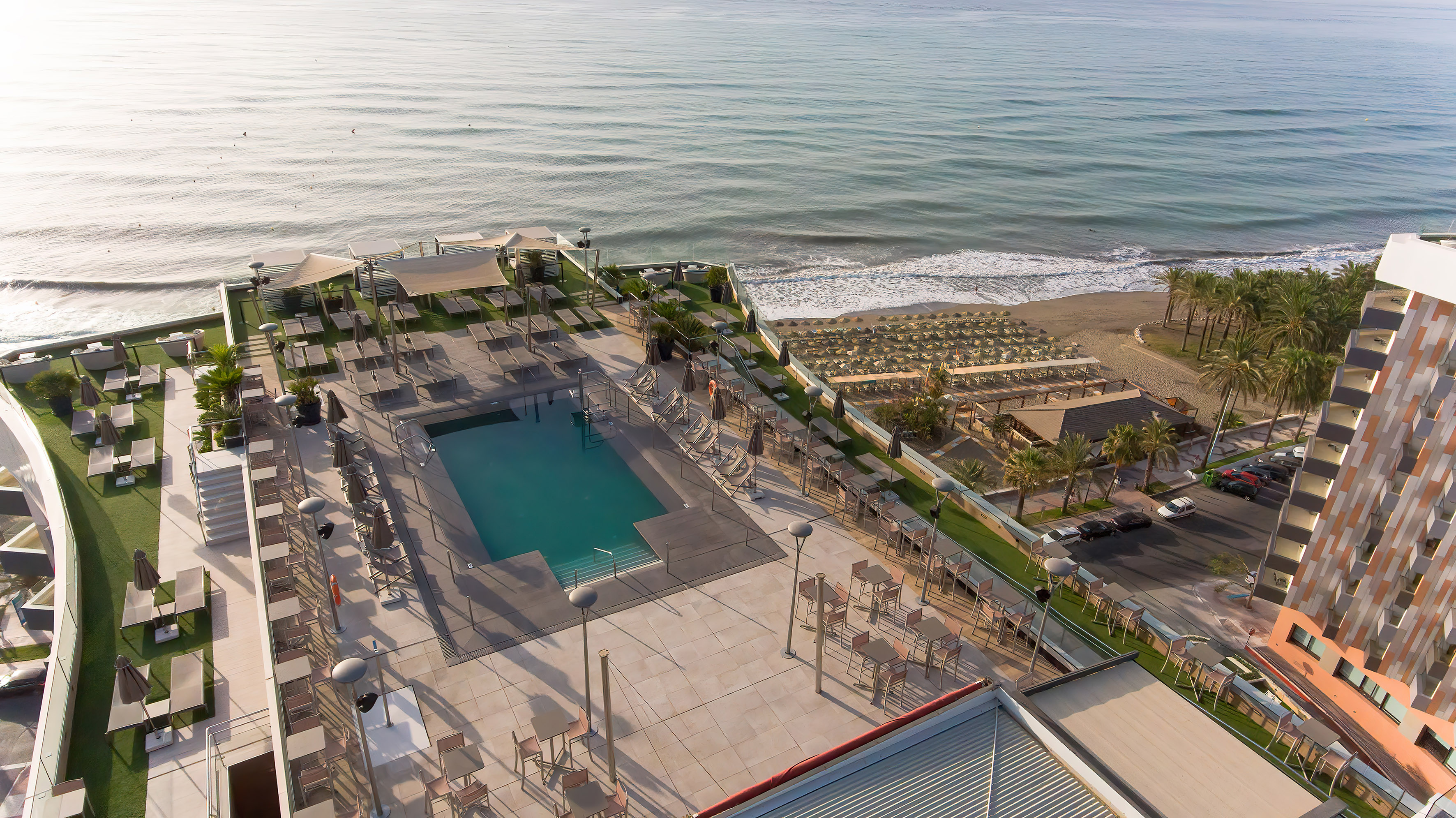 a pool and chairs on a rooftop overlooking a beach