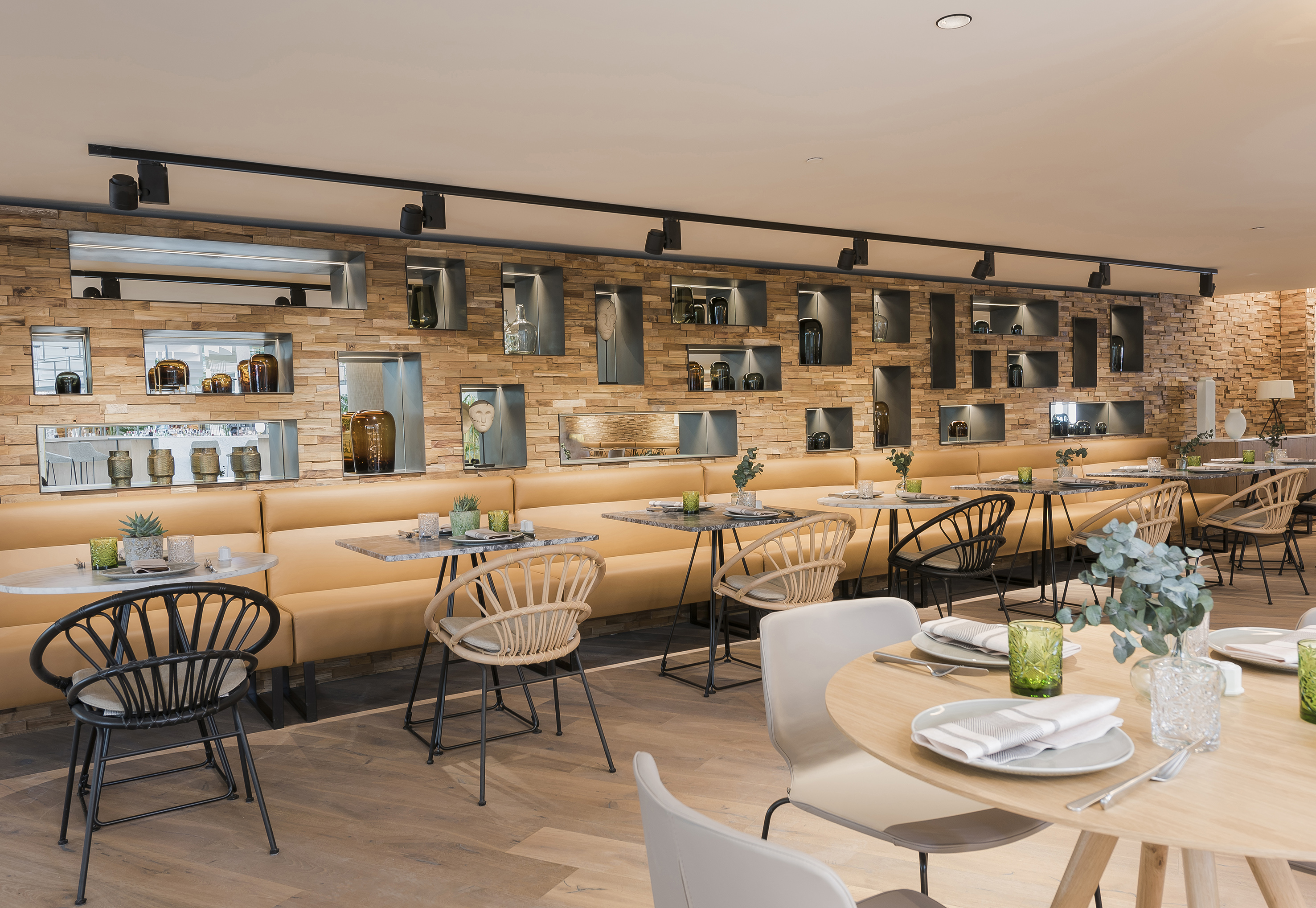 Modern restaurant dining with wood wall, tan booths, marble tables, and wicker chairs.