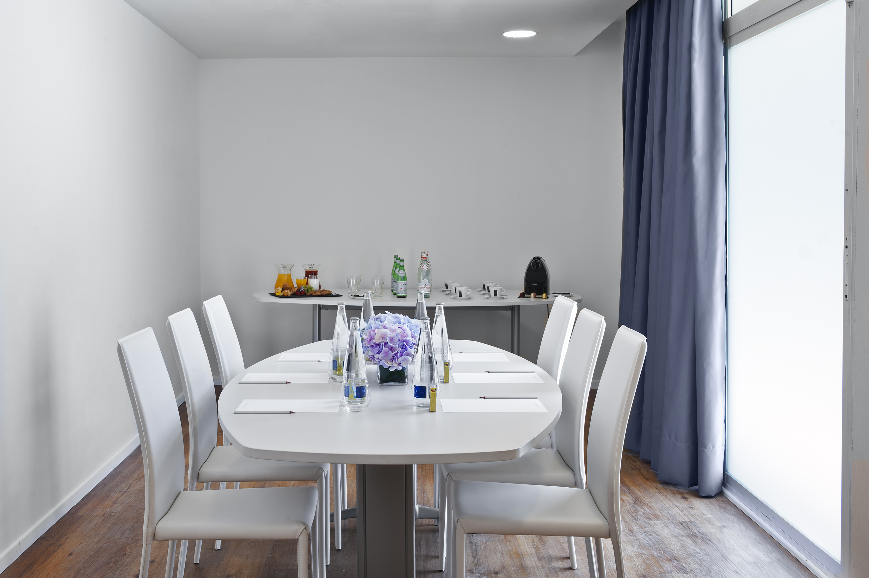 Modern conference room with oval table, white chairs, and refreshments.