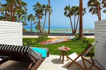 a deck chairs and a table on a patio with palm trees and a beach