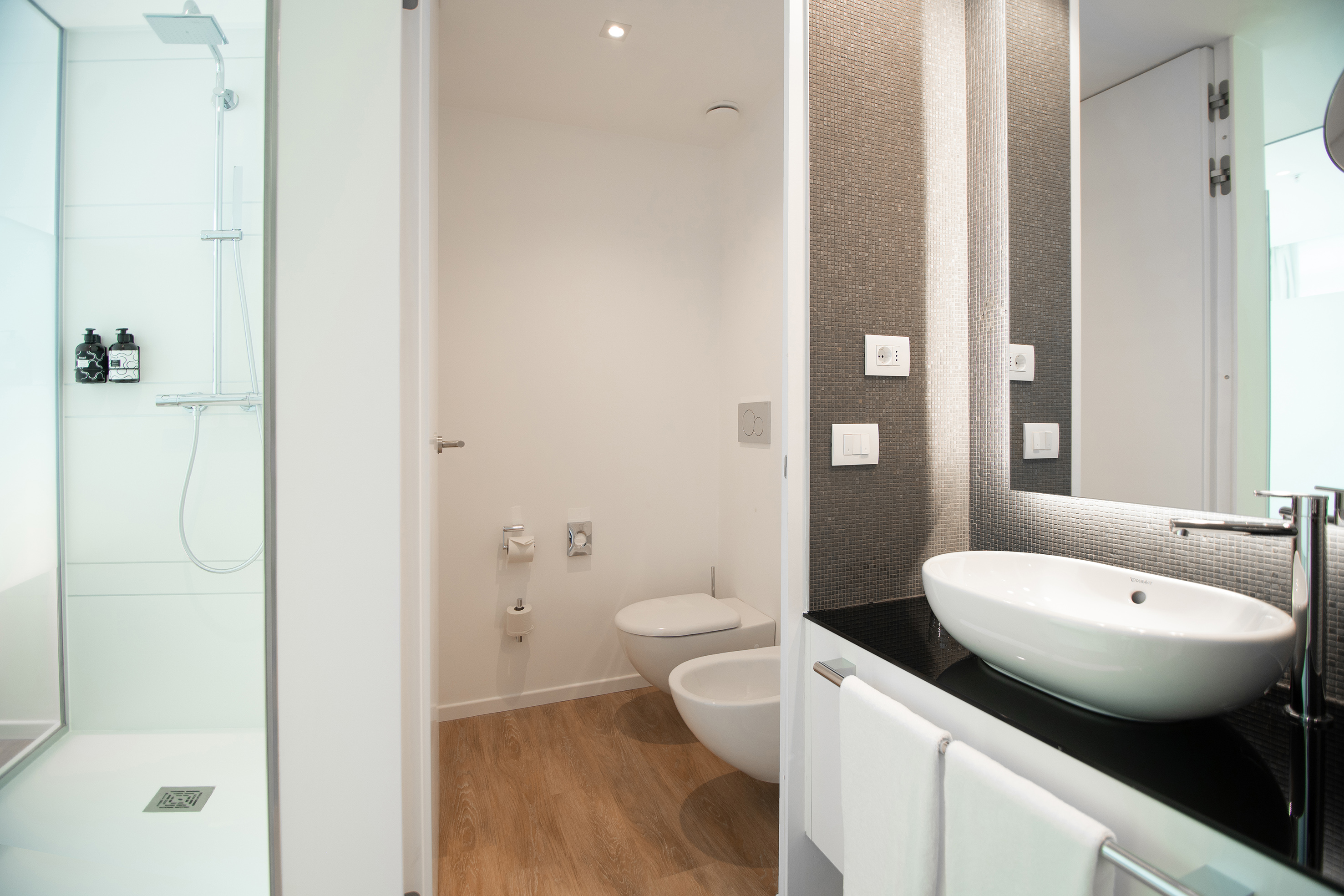 Modern bathroom with walk-in shower, toilet, bidet, and vessel sink.