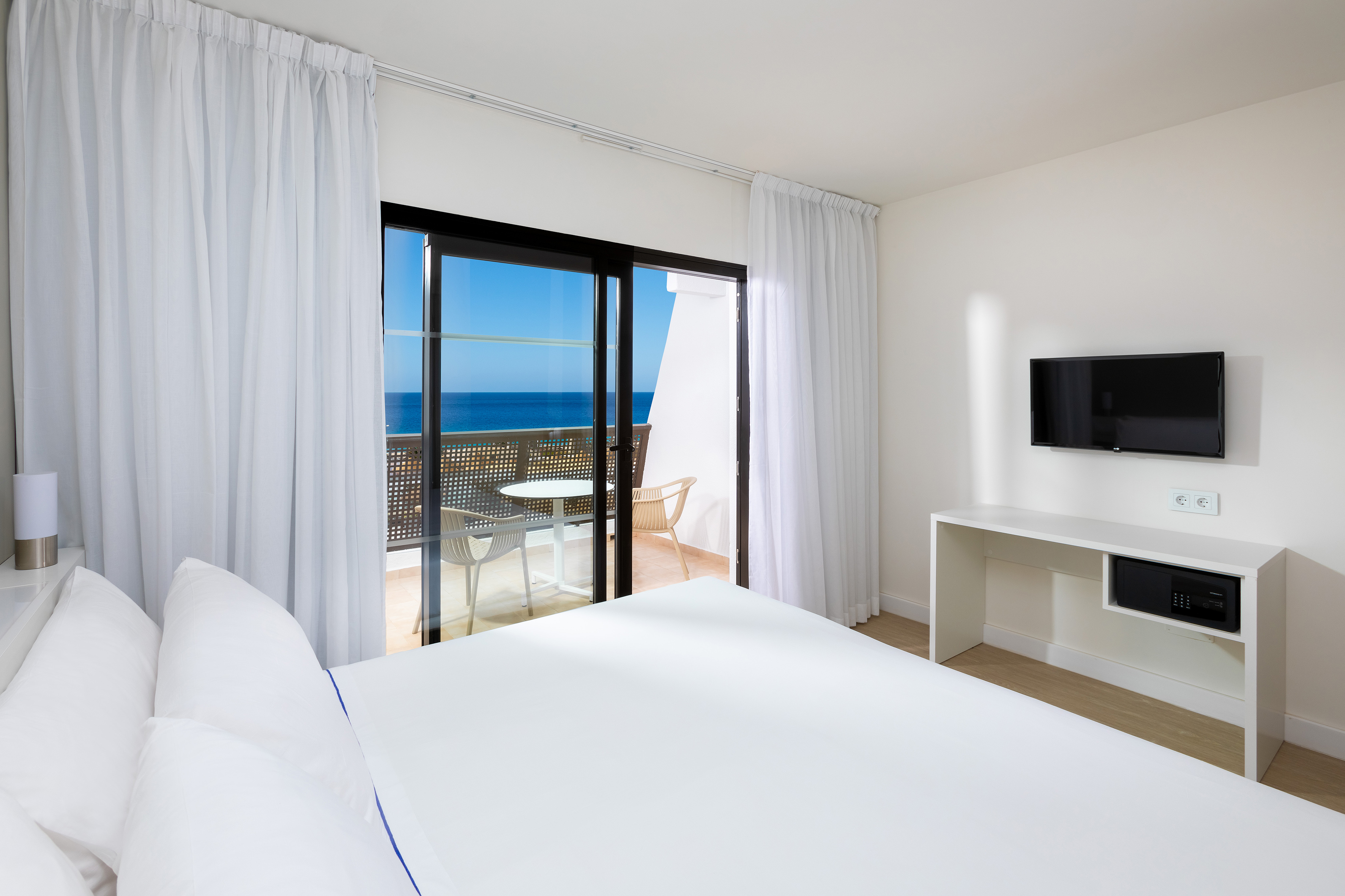 Bright hotel room with sea view balcony, white bedding, and flat-screen TV.