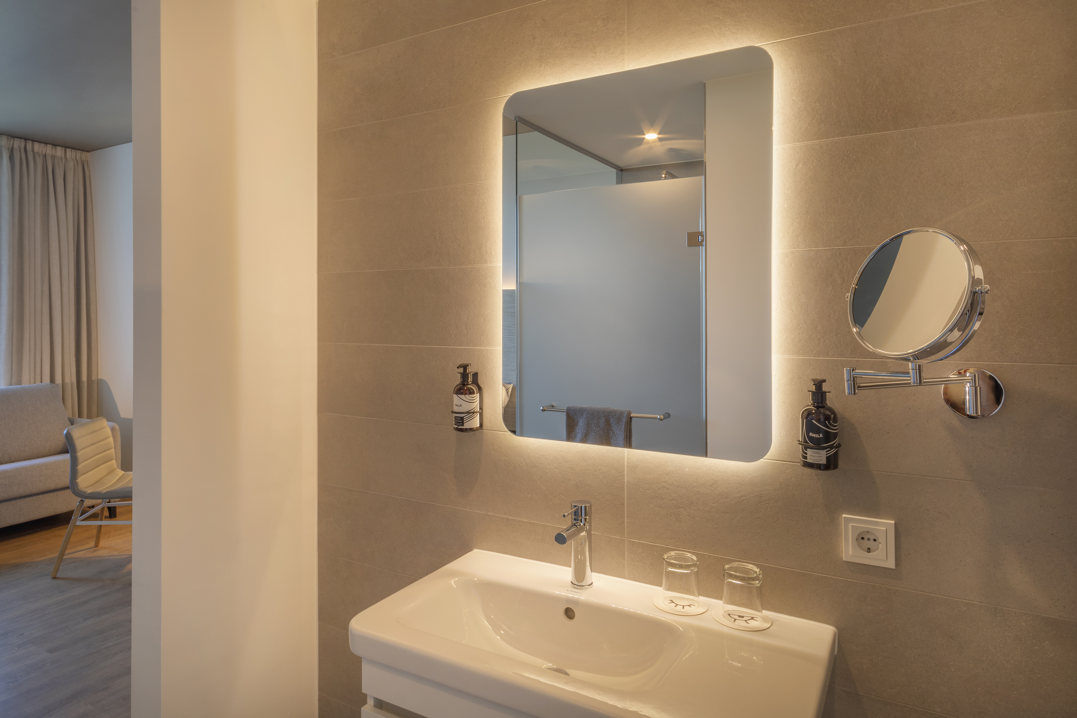 Contemporary hotel bathroom with illuminated mirror, sink, and magnifying mirror.