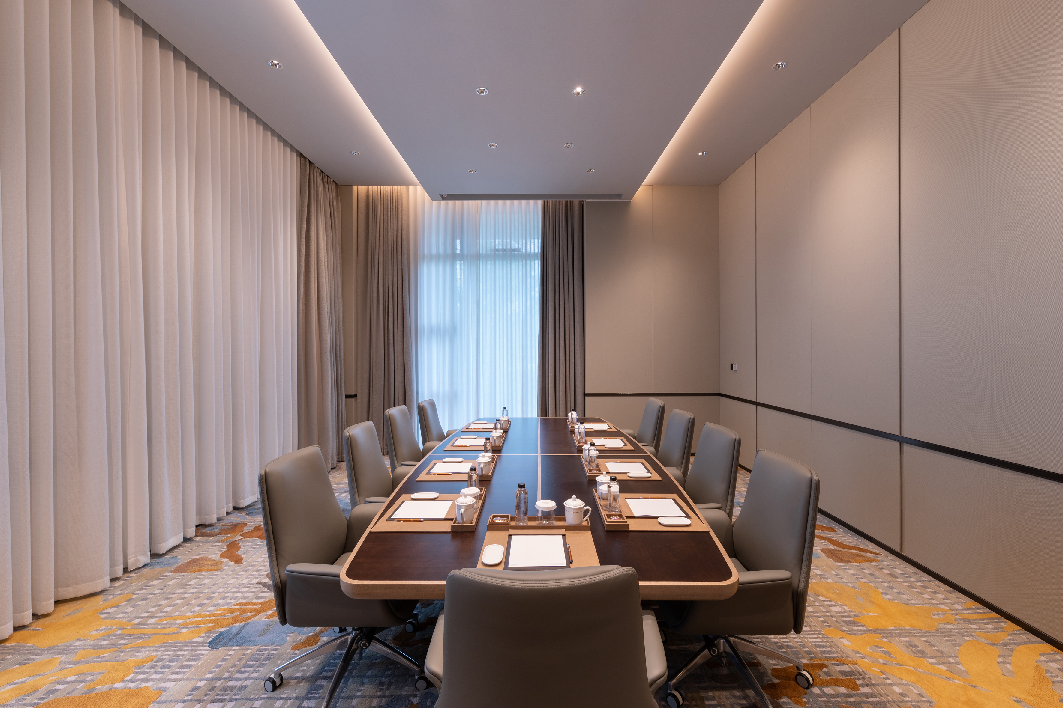 Modern boardroom with large wooden table, executive chairs, patterned carpet.