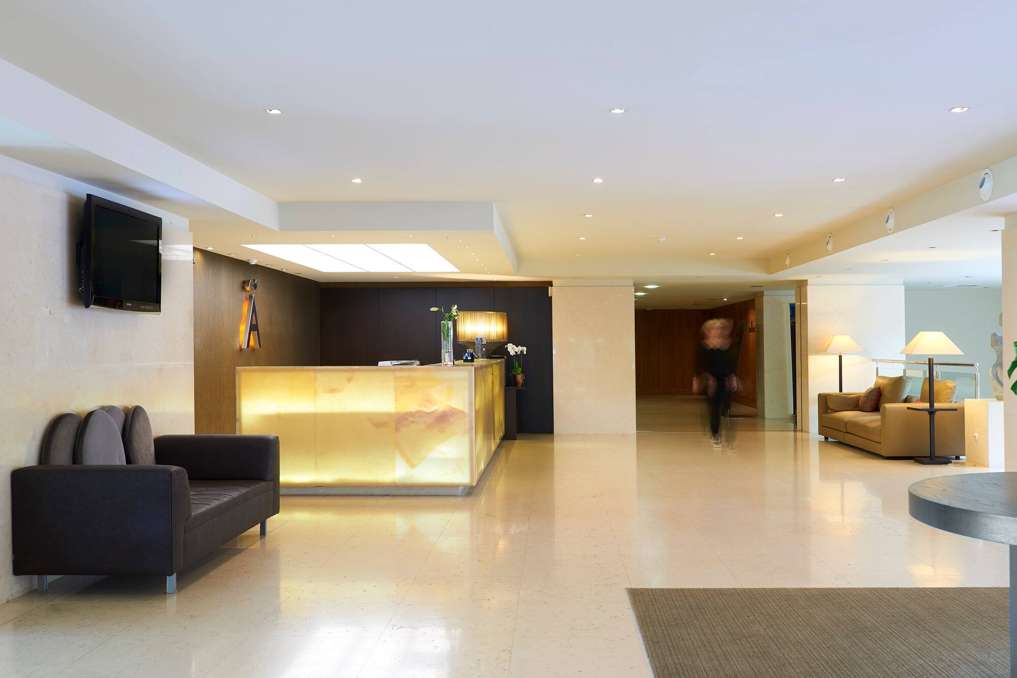 Modern hotel lobby with illuminated reception desk and comfortable seating.