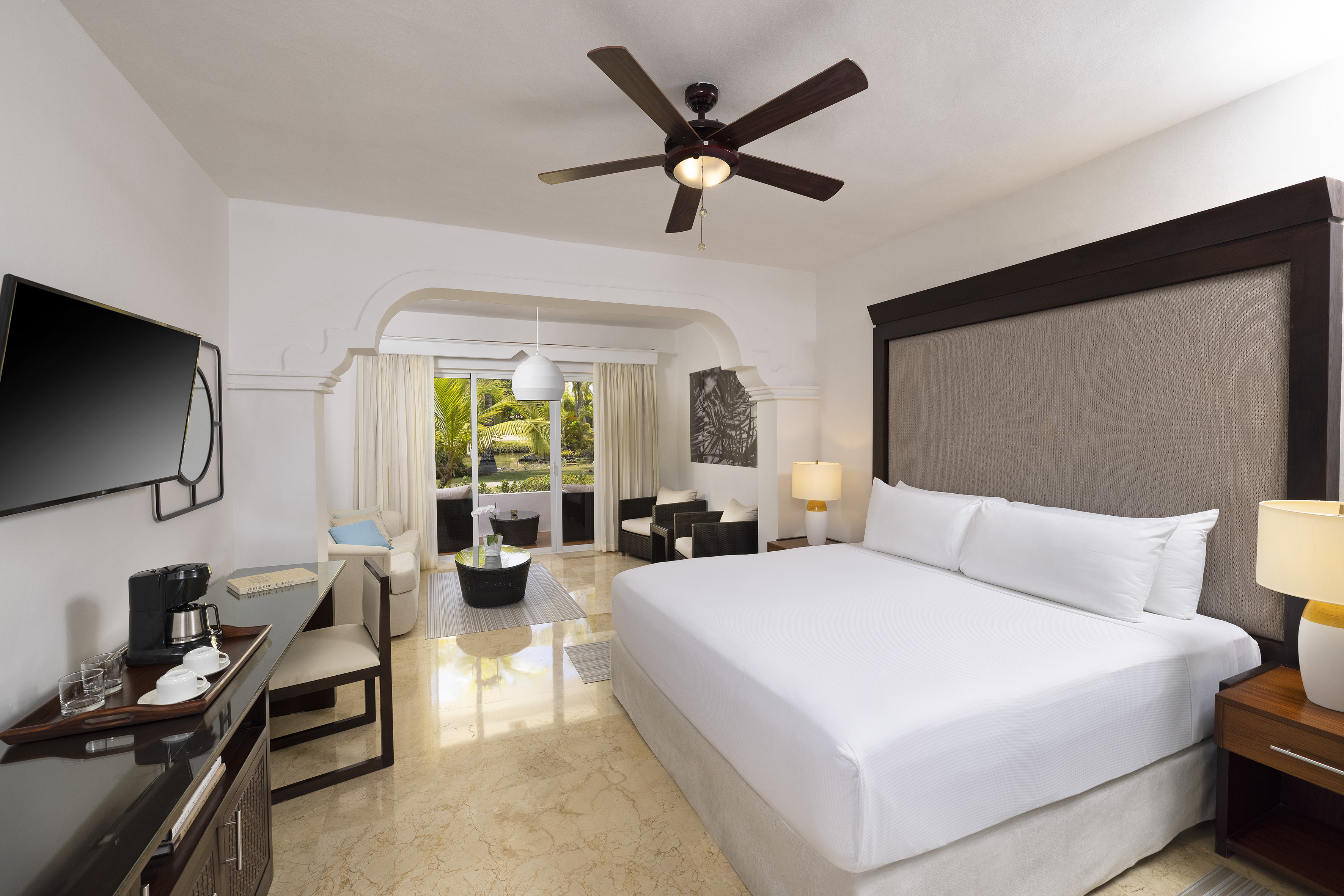 Spacious hotel suite with king bed, living area, and tropical balcony view.