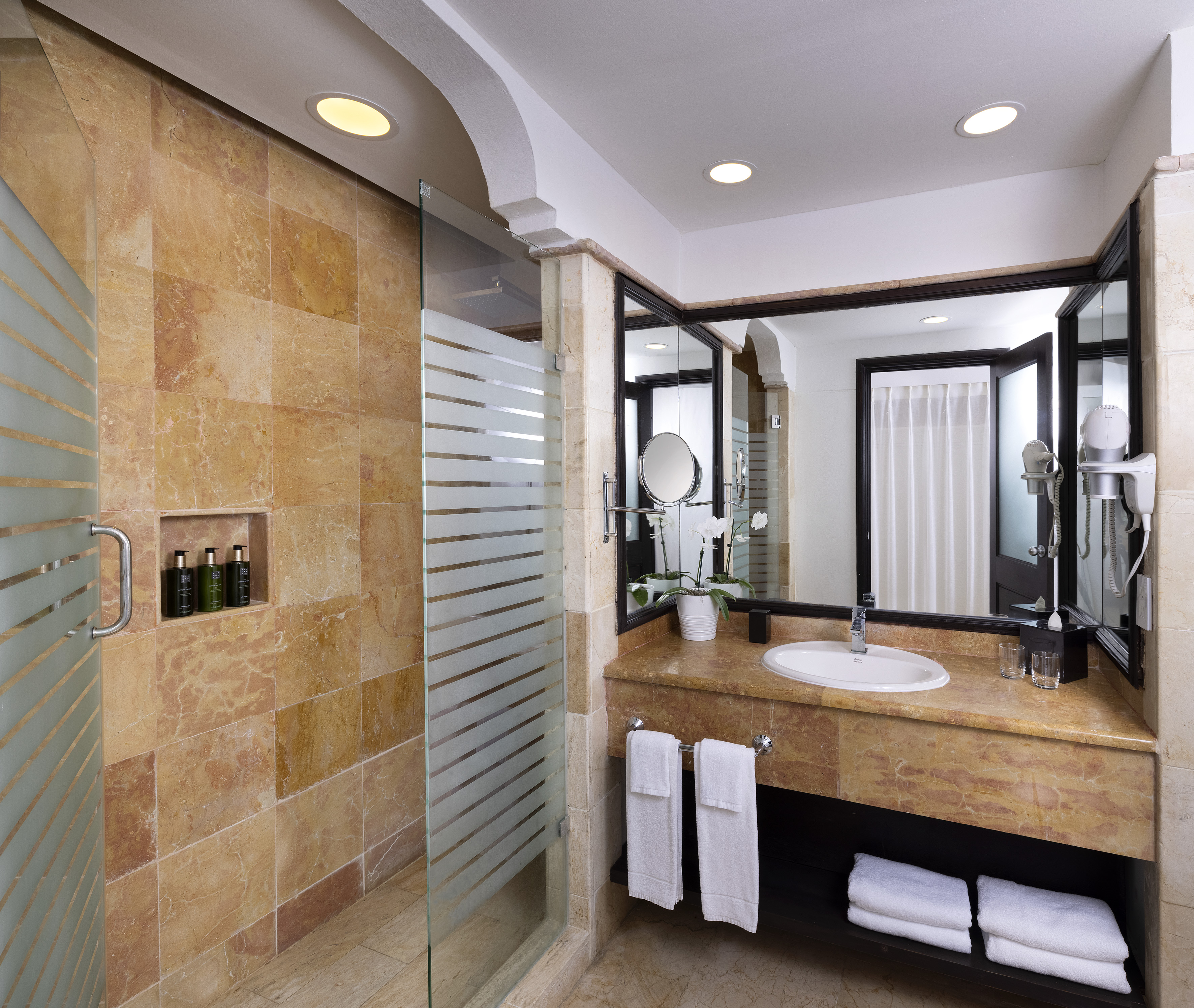 Hotel bathroom with marble vanity, tiled shower, and large mirror.