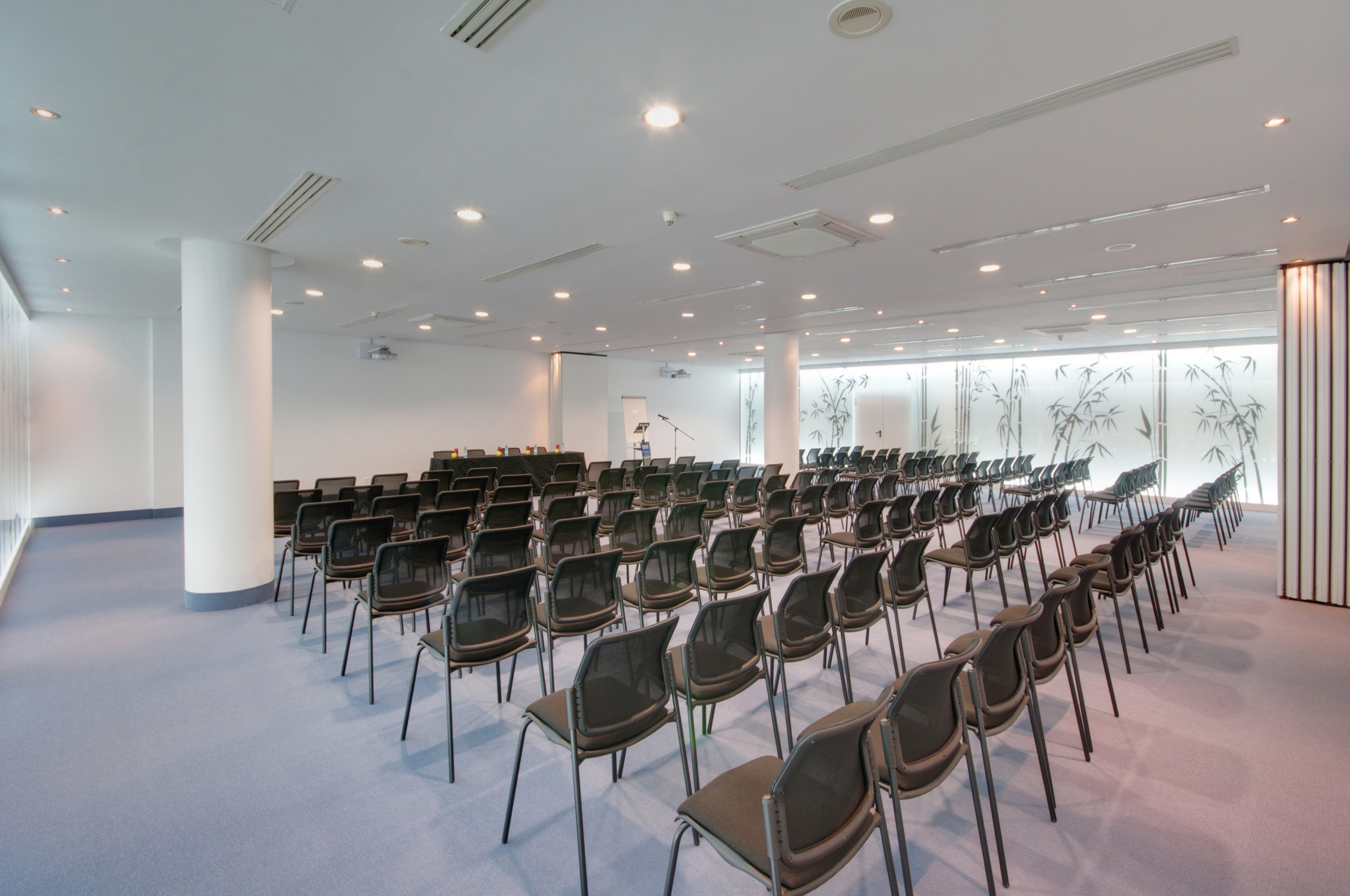 Conference room with rows of empty chairs, projector screen, and frosted bamboo windows.
