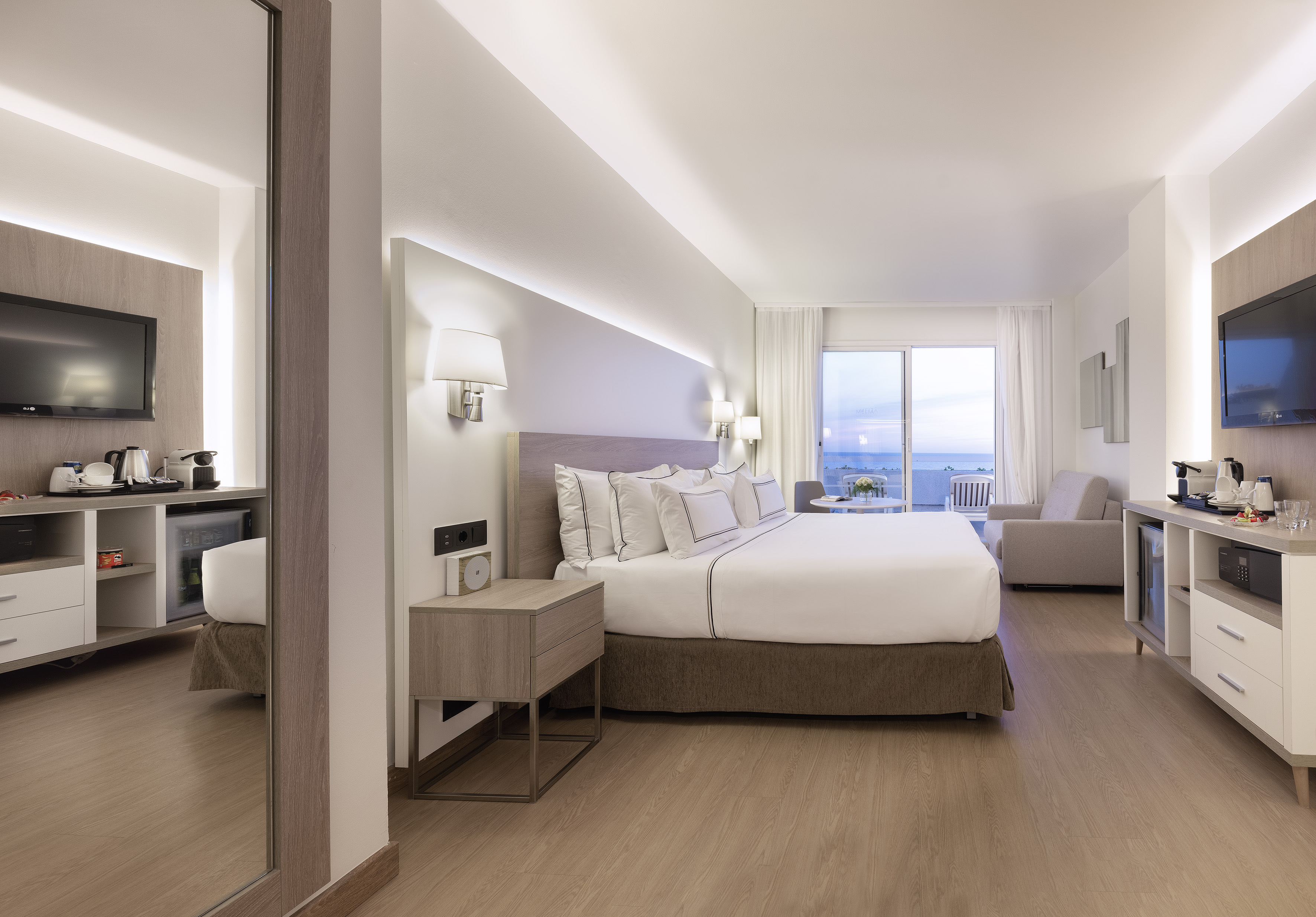 Luxury hotel bedroom featuring king bed, balcony with sea view, and modern amenities.
