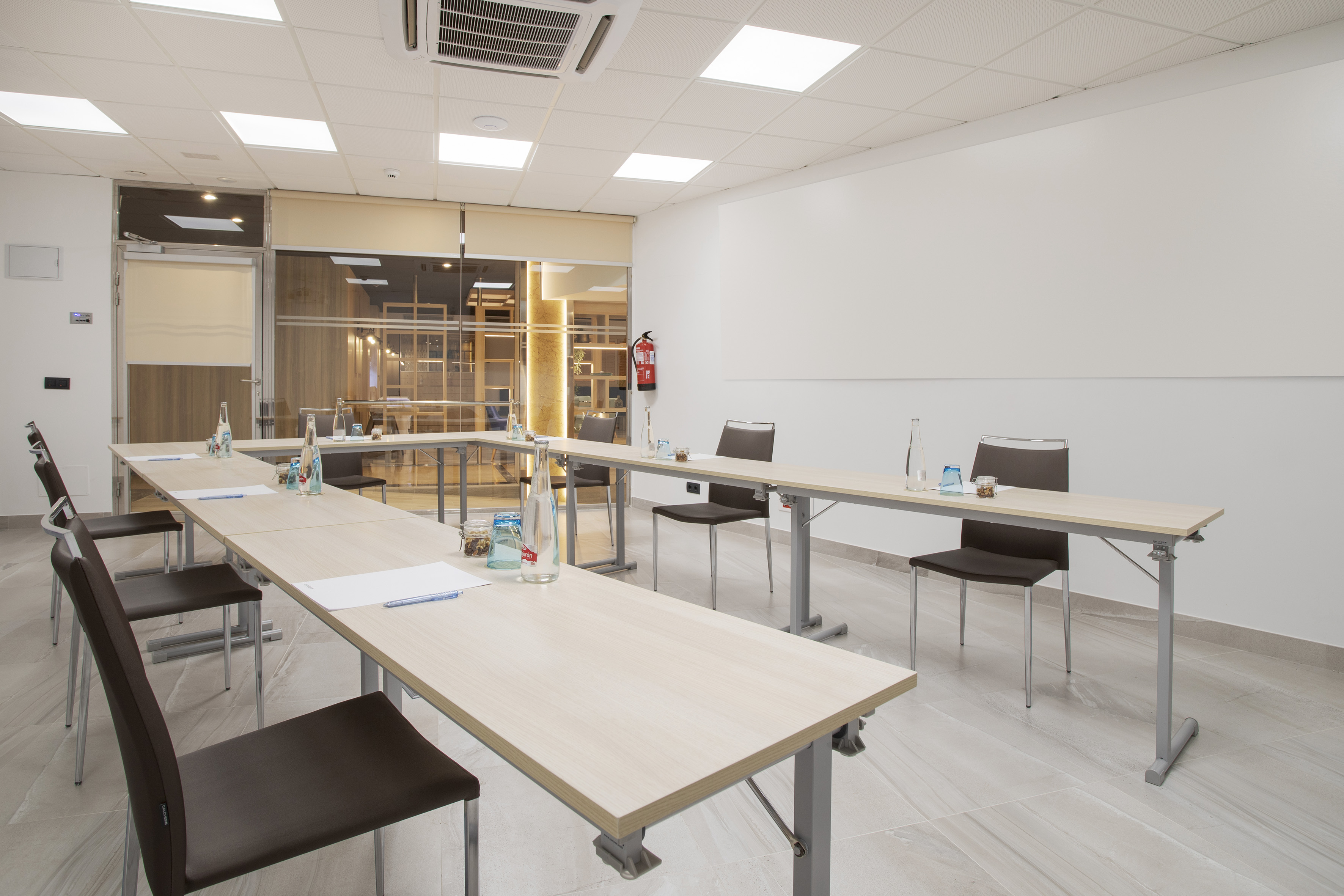 Modern U-shape conference room with tables, chairs, and presentation wall.
