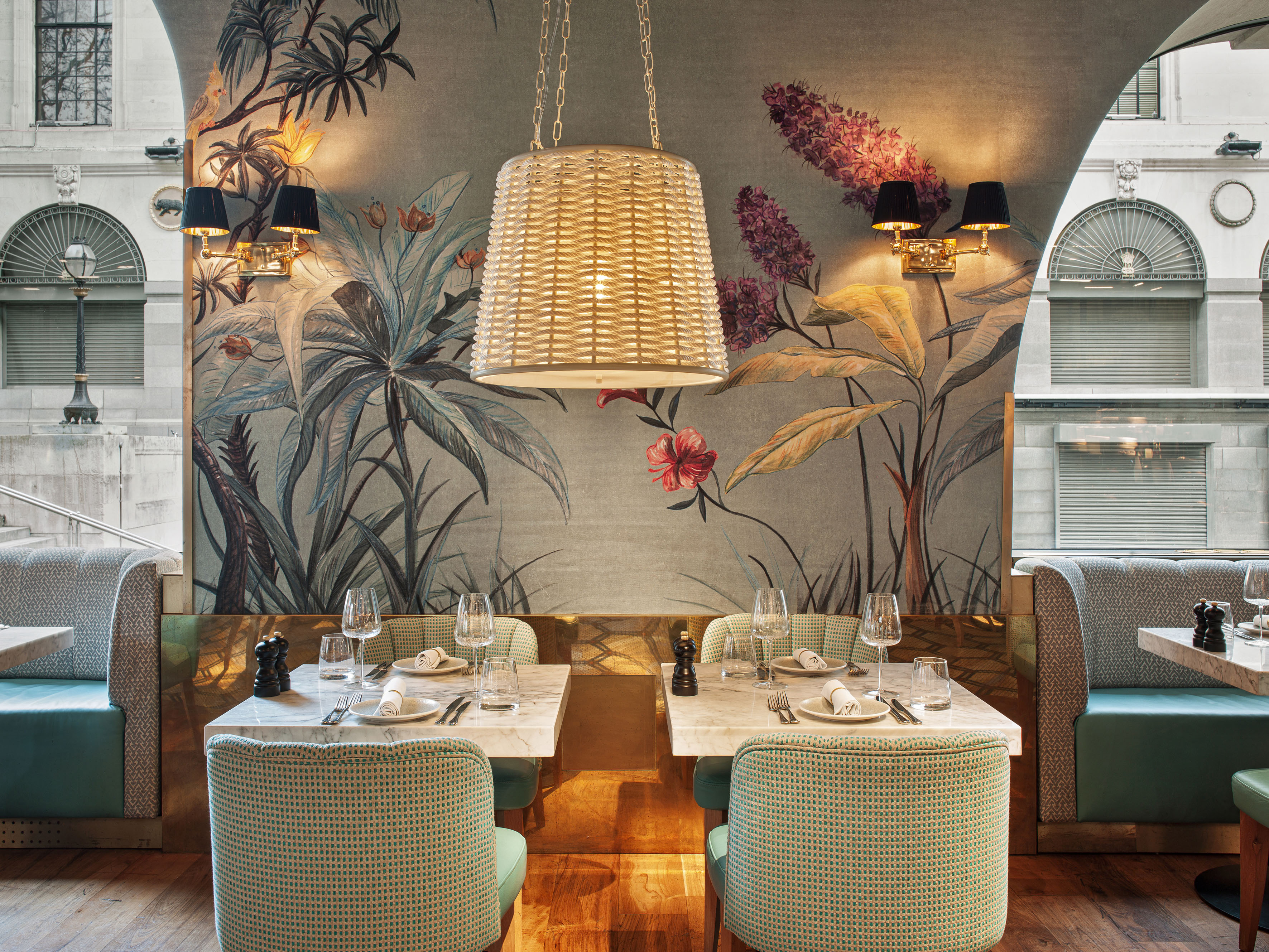 Restaurant dining room with tropical wallpaper, marble tables, and green seating.