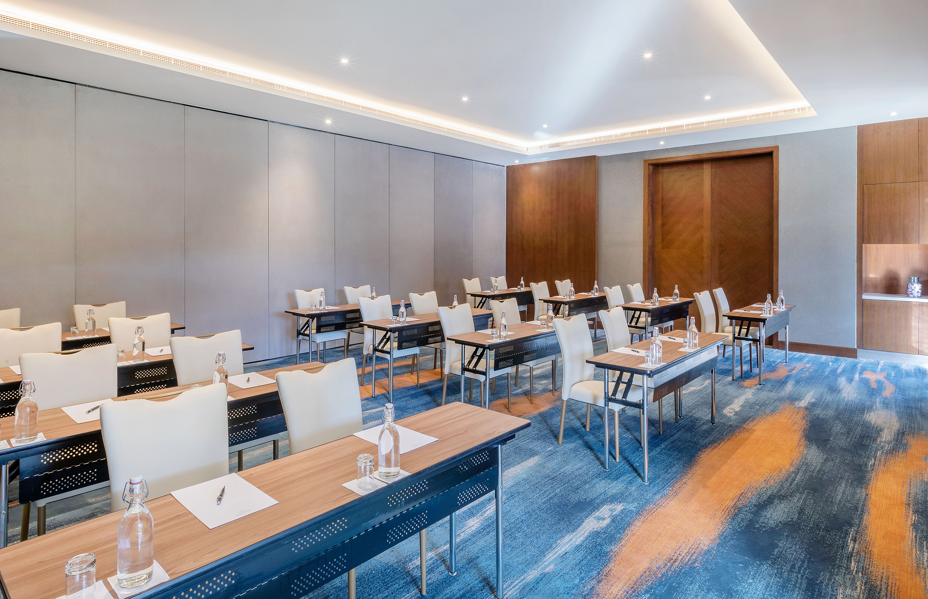 Modern conference room with individual tables, white chairs, and abstract blue carpet.