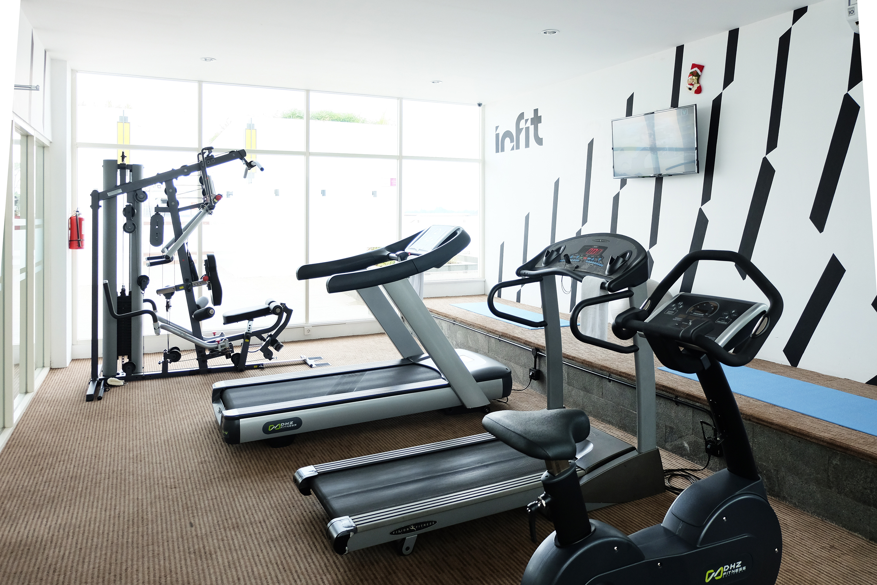 Hotel gym with treadmills, exercise bike, and weight machine by large windows.