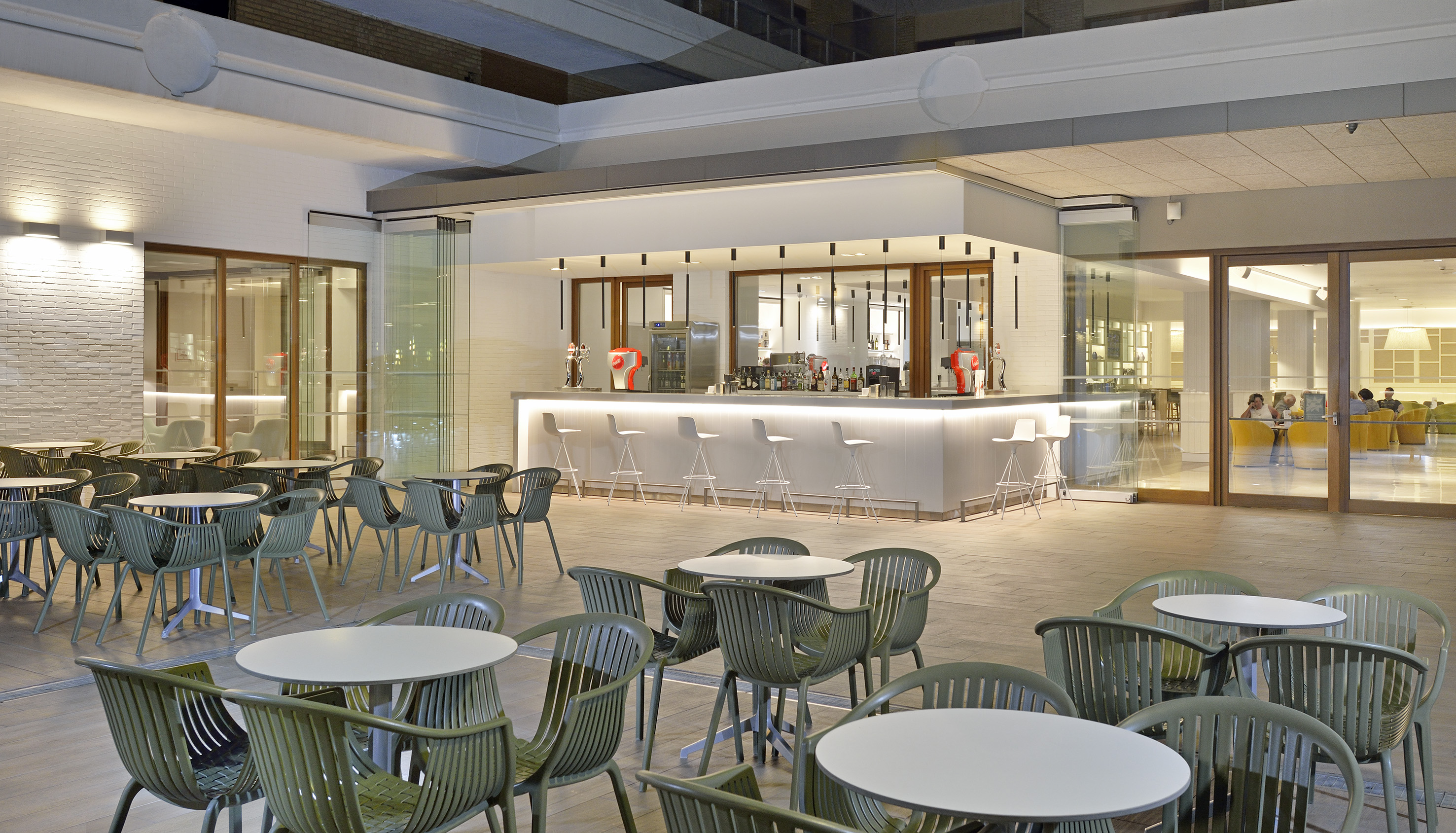 Modern hotel bar with white counter and green outdoor cafe seating.