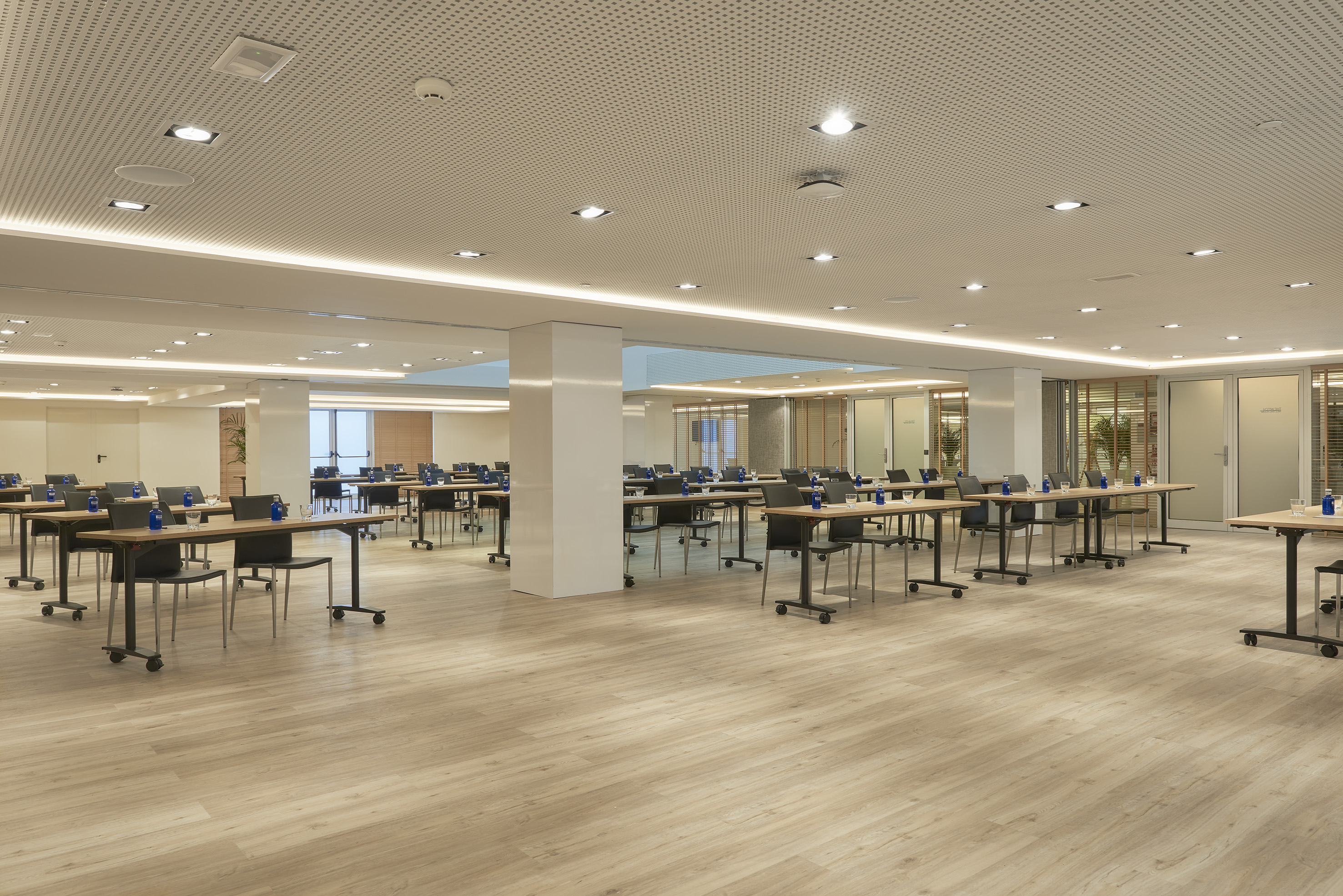 Modern meeting room with rows of tables, chairs, and light wood floor.