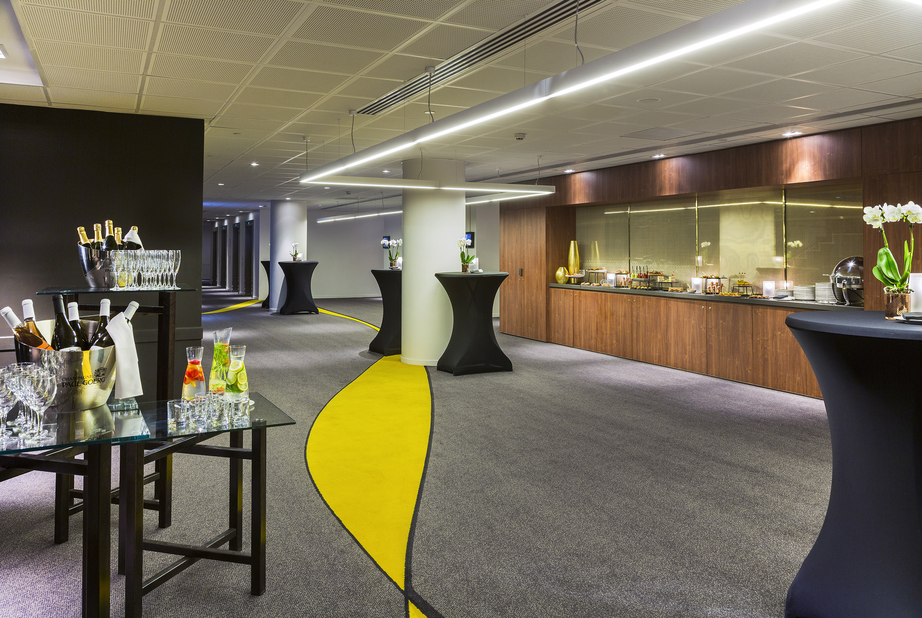 Contemporary event space with buffet, champagne, cocktails, and yellow carpet.