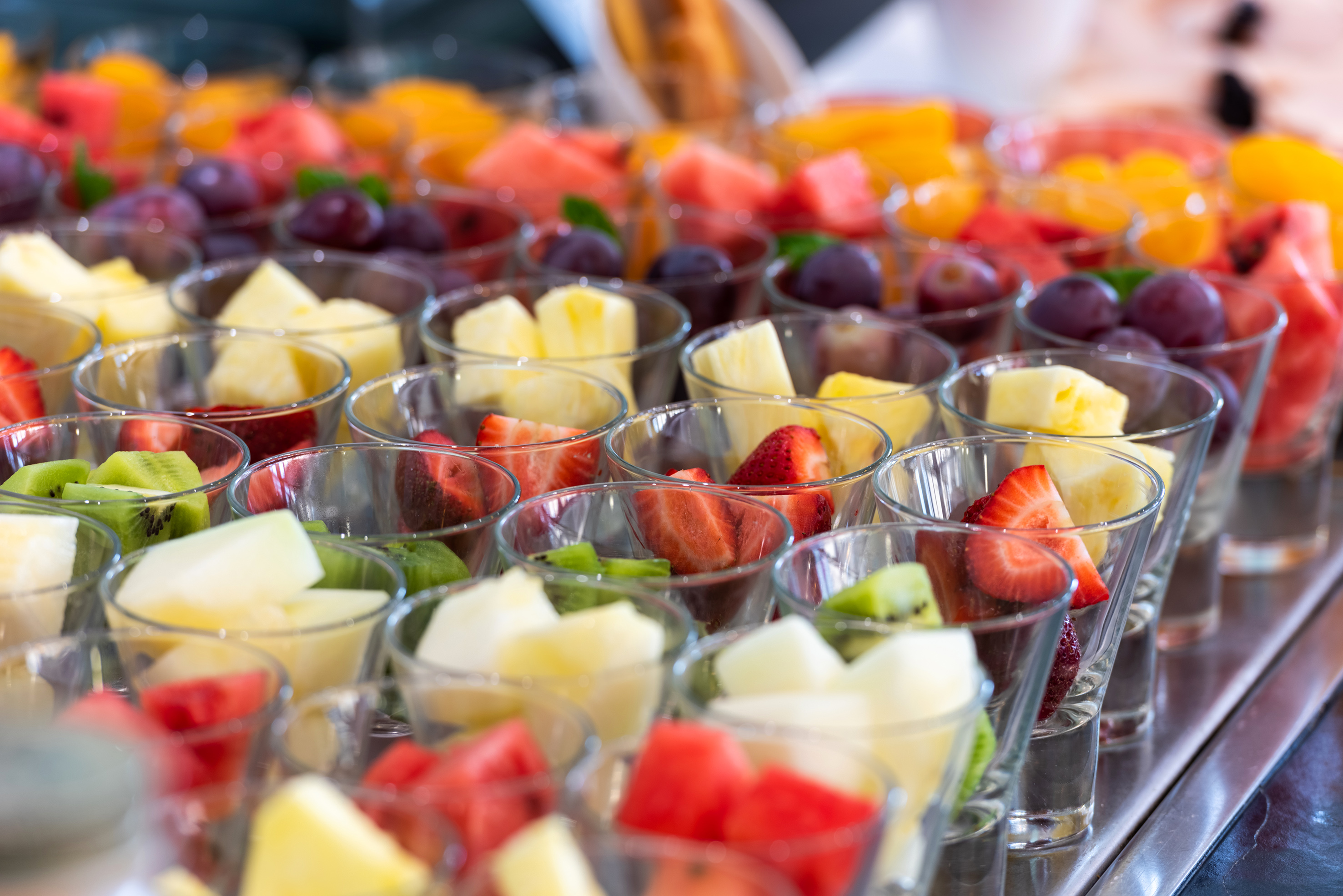 Fresh fruit salad cups, buffet style, with strawberries, pineapple, kiwi, and grapes.