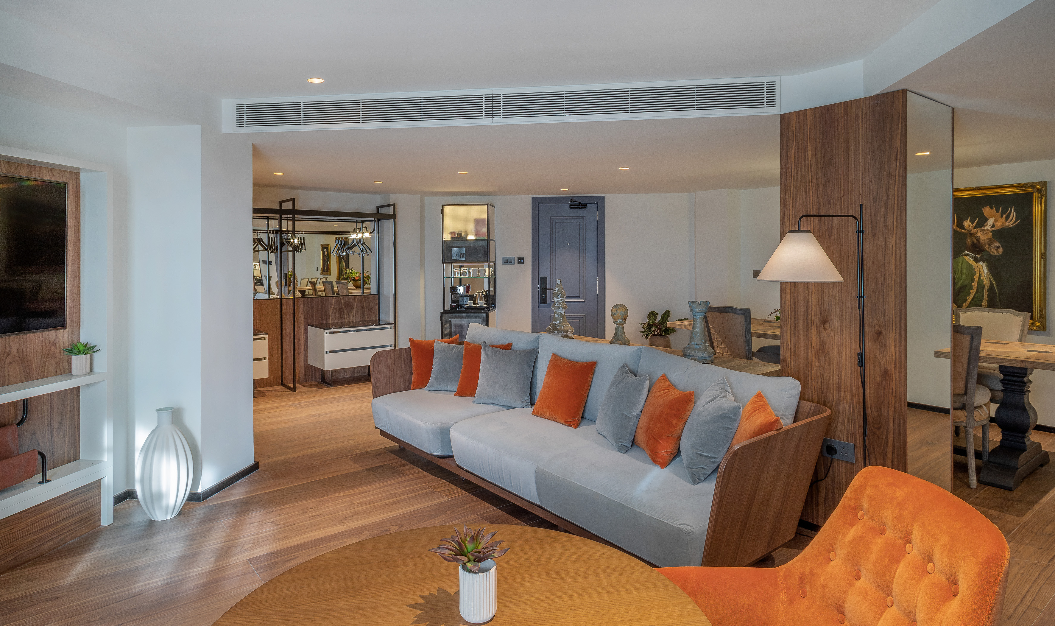 Modern living room with gray sofa, orange accents, wood floor, and dining area.