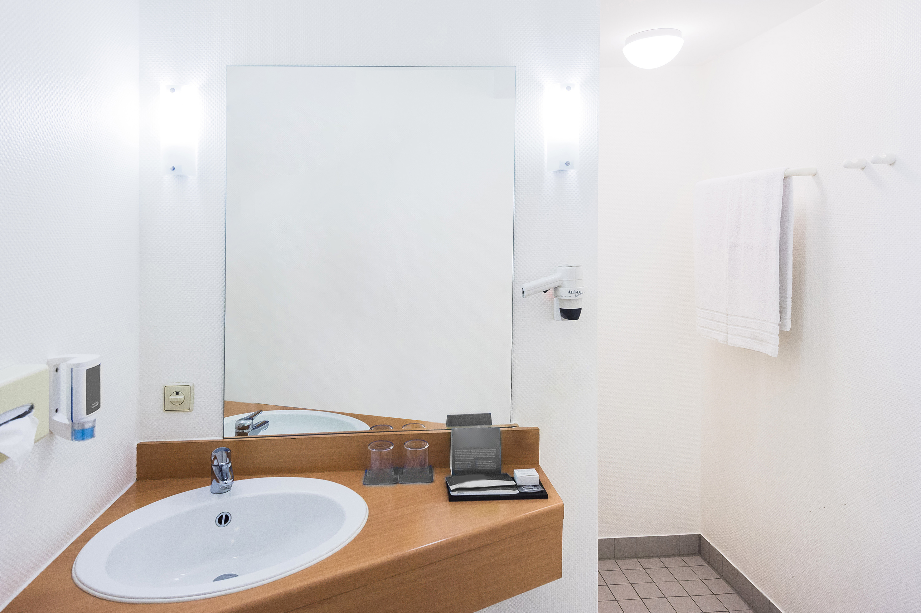 Hotel bathroom with white sink, large mirror, wooden vanity, hairdryer, and towels.