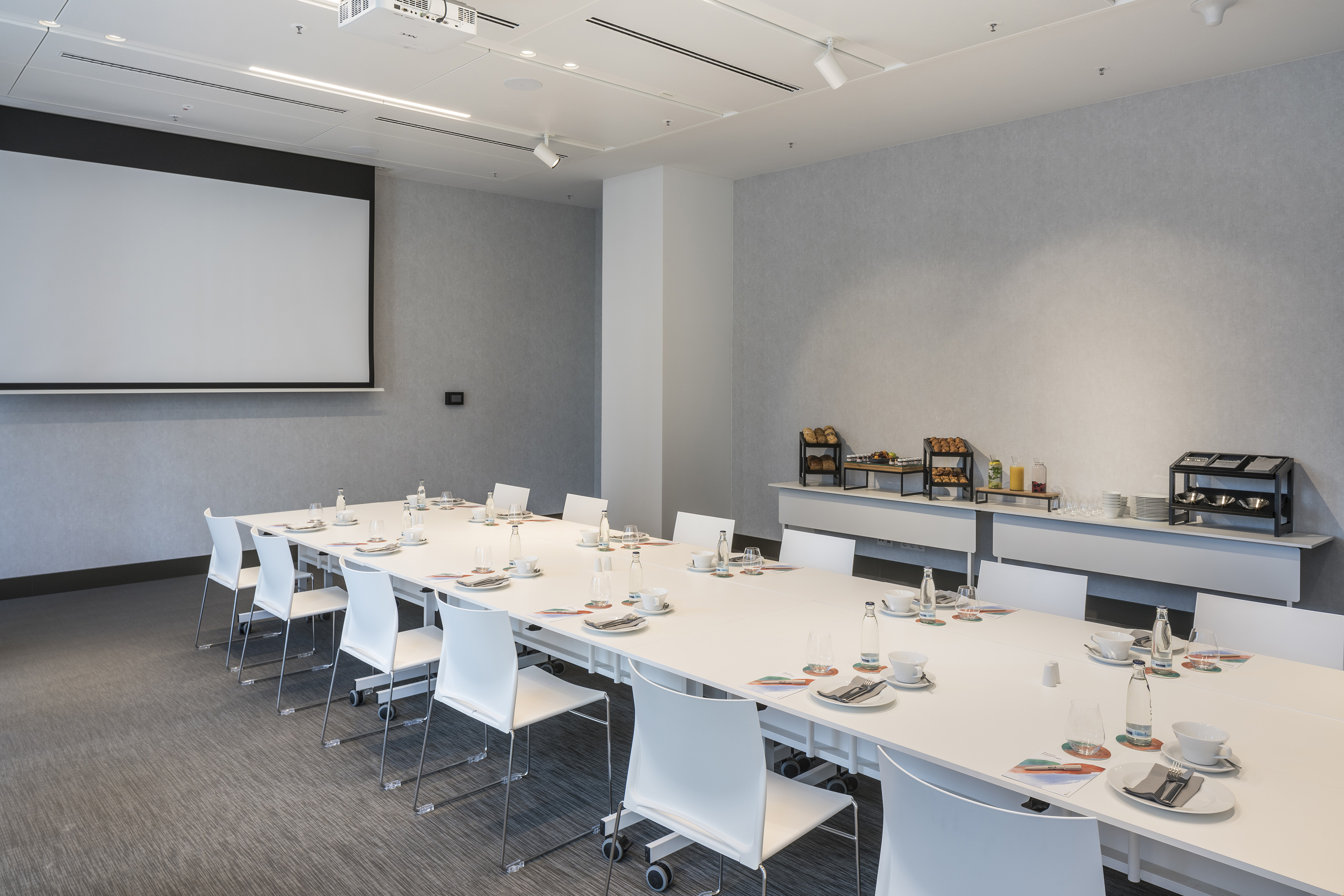 Modern conference room with projector screen, long table, and refreshment bar.