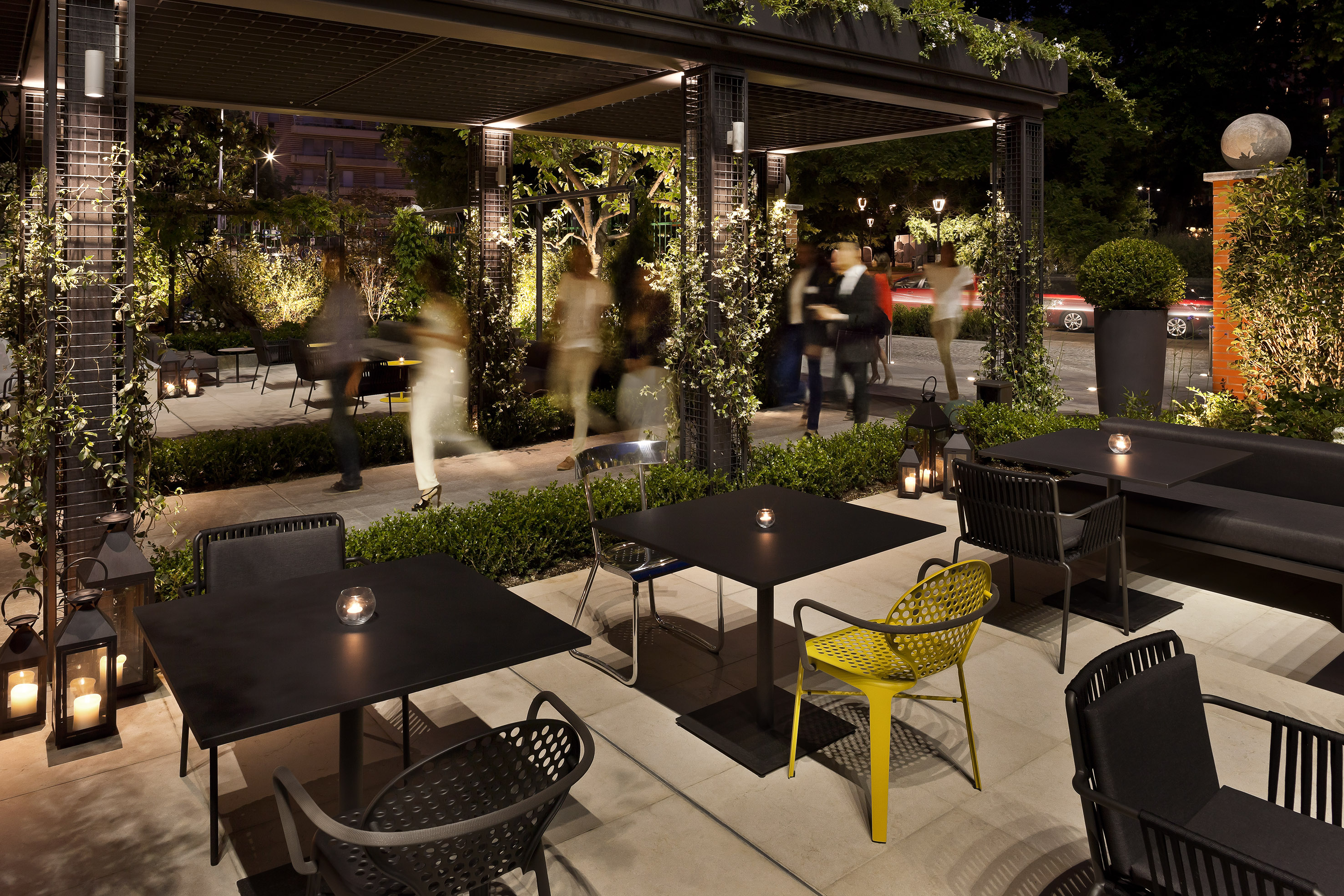 Outdoor restaurant patio at night with modern tables, illuminated pergola.