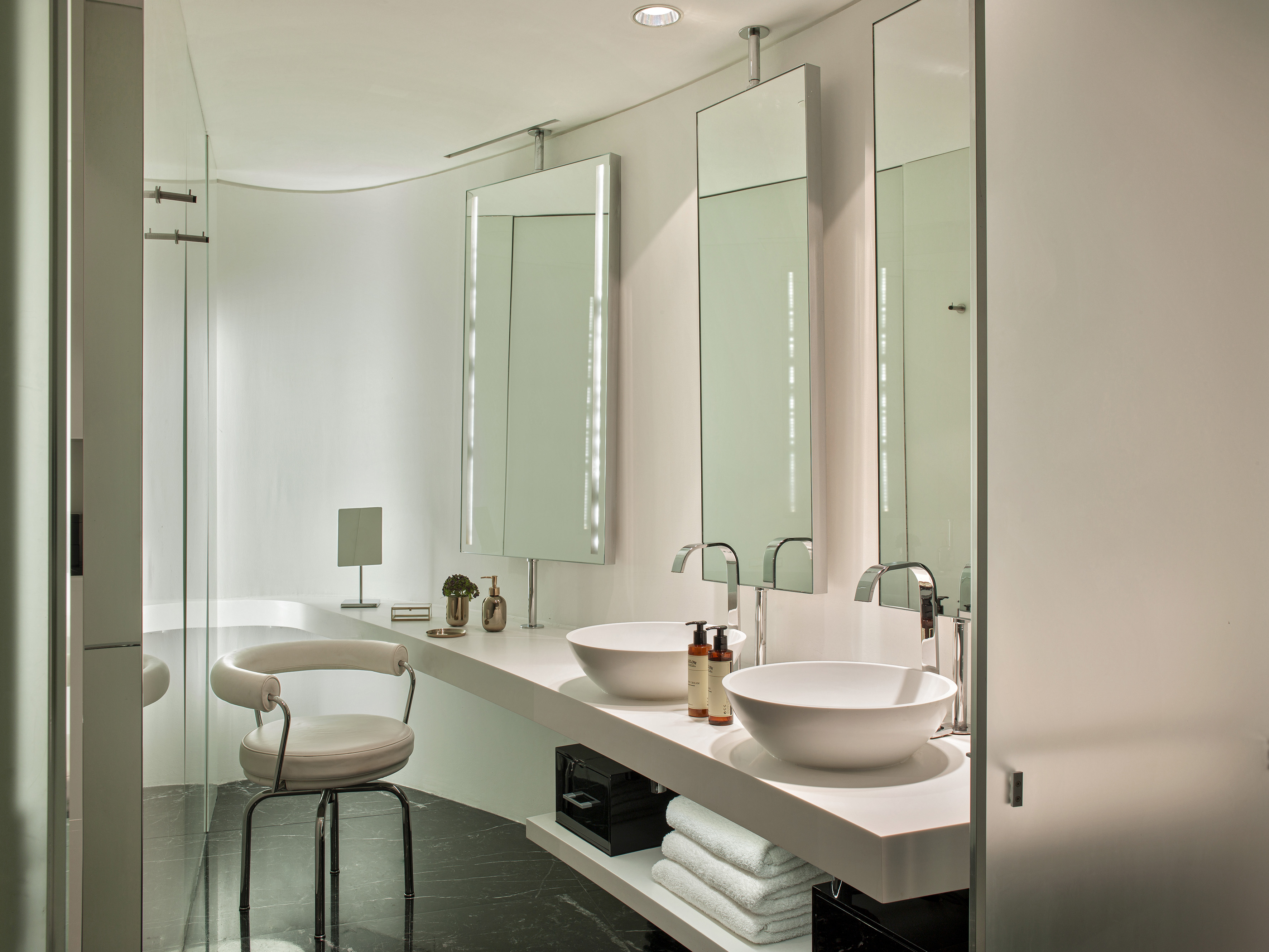 Modern bathroom with double vessel sinks, illuminated mirrors, and white vanity.