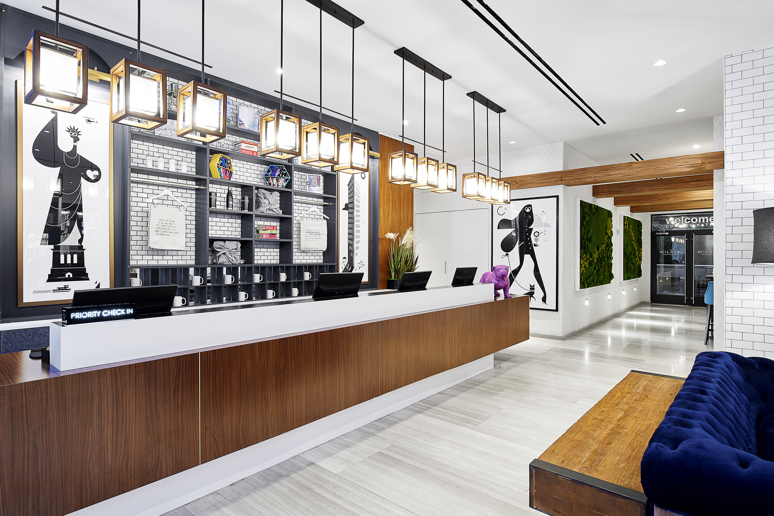 Modern hotel lobby with wood reception desk, pendant lights, art, and blue sofa. - INNSiDE New York NoMad, Nueva York