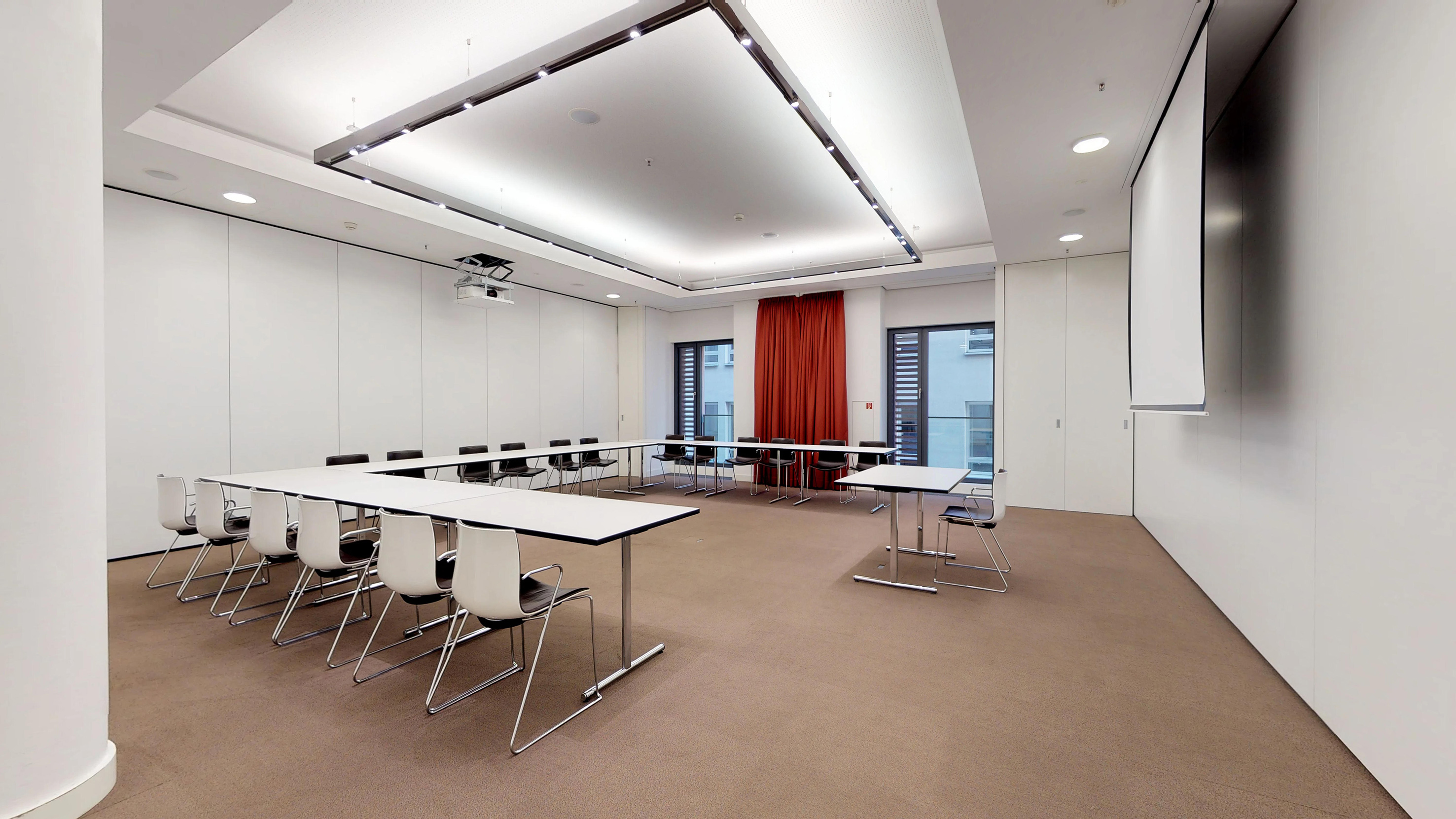 Modern meeting room with U-shaped tables, projector, and screen.