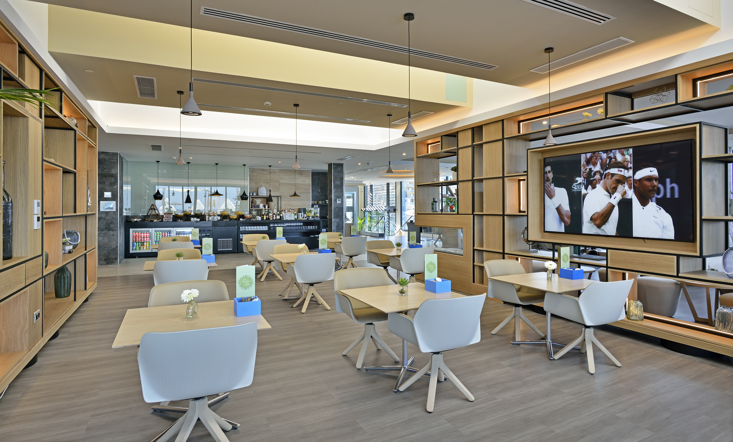 Modern dining lounge with buffet, wood tables, chairs, and large TV displaying tennis.