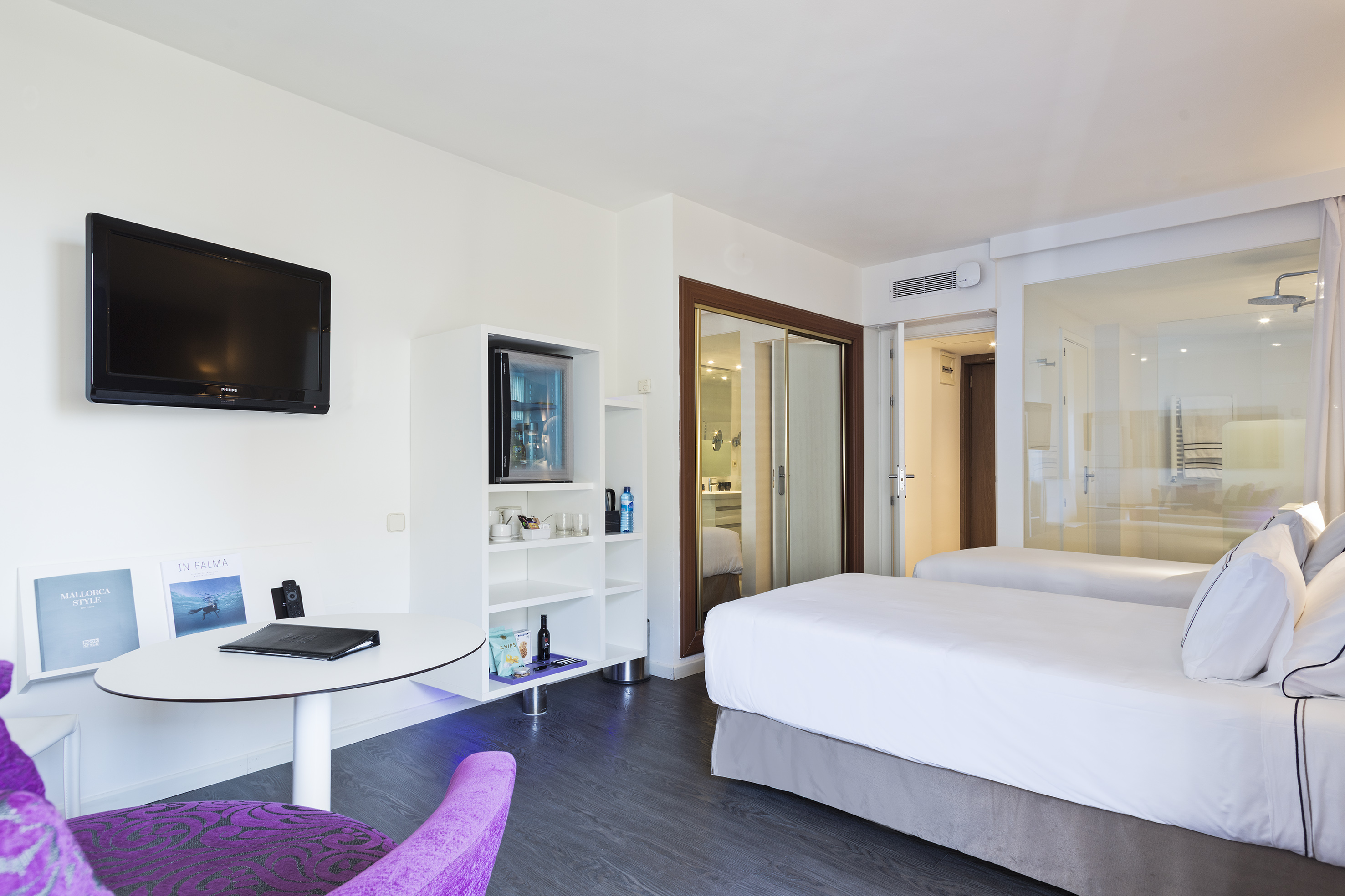 Modern guest room with two beds, TV, minibar, and glass shower.