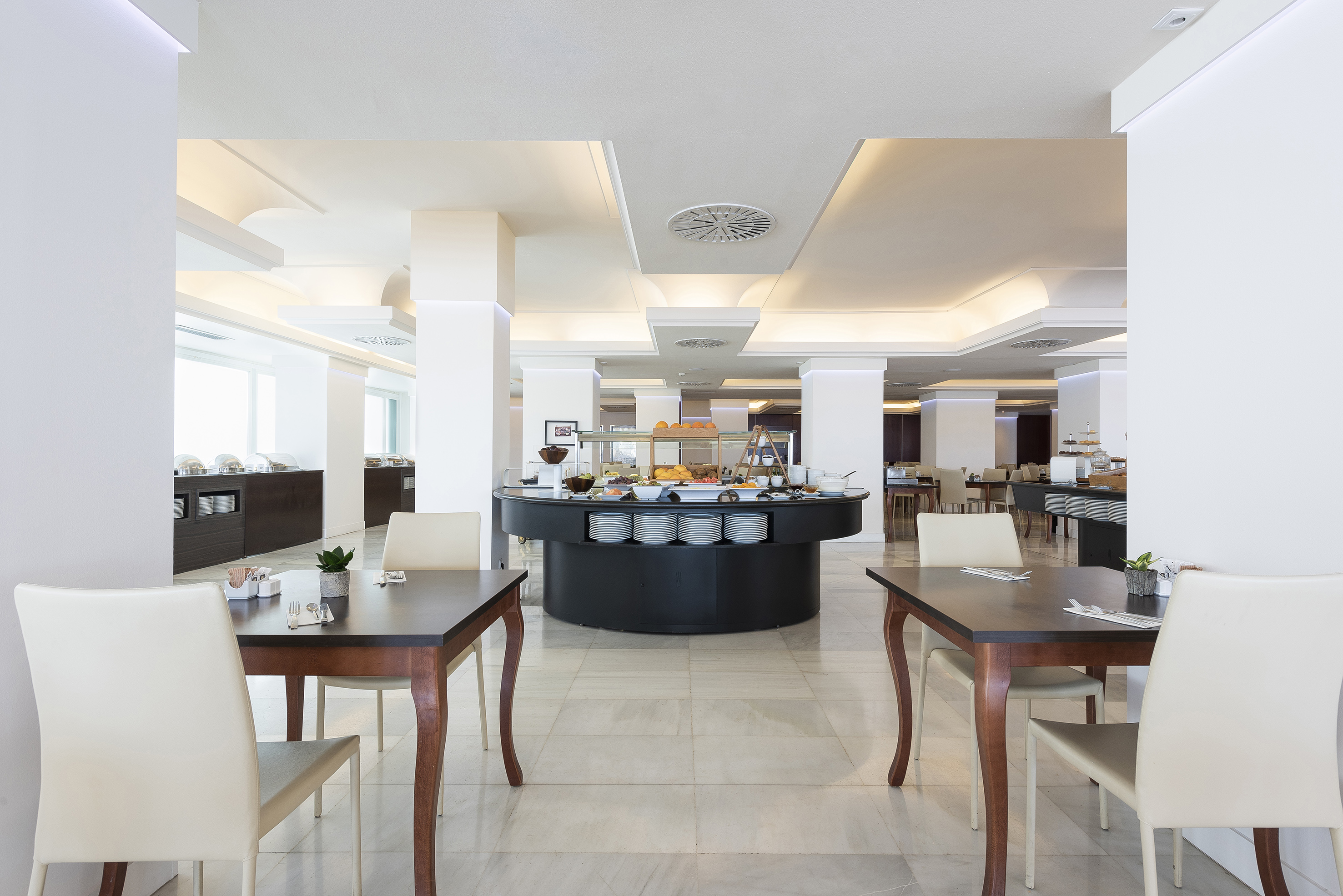 Modern hotel buffet restaurant with breakfast display and dining tables.