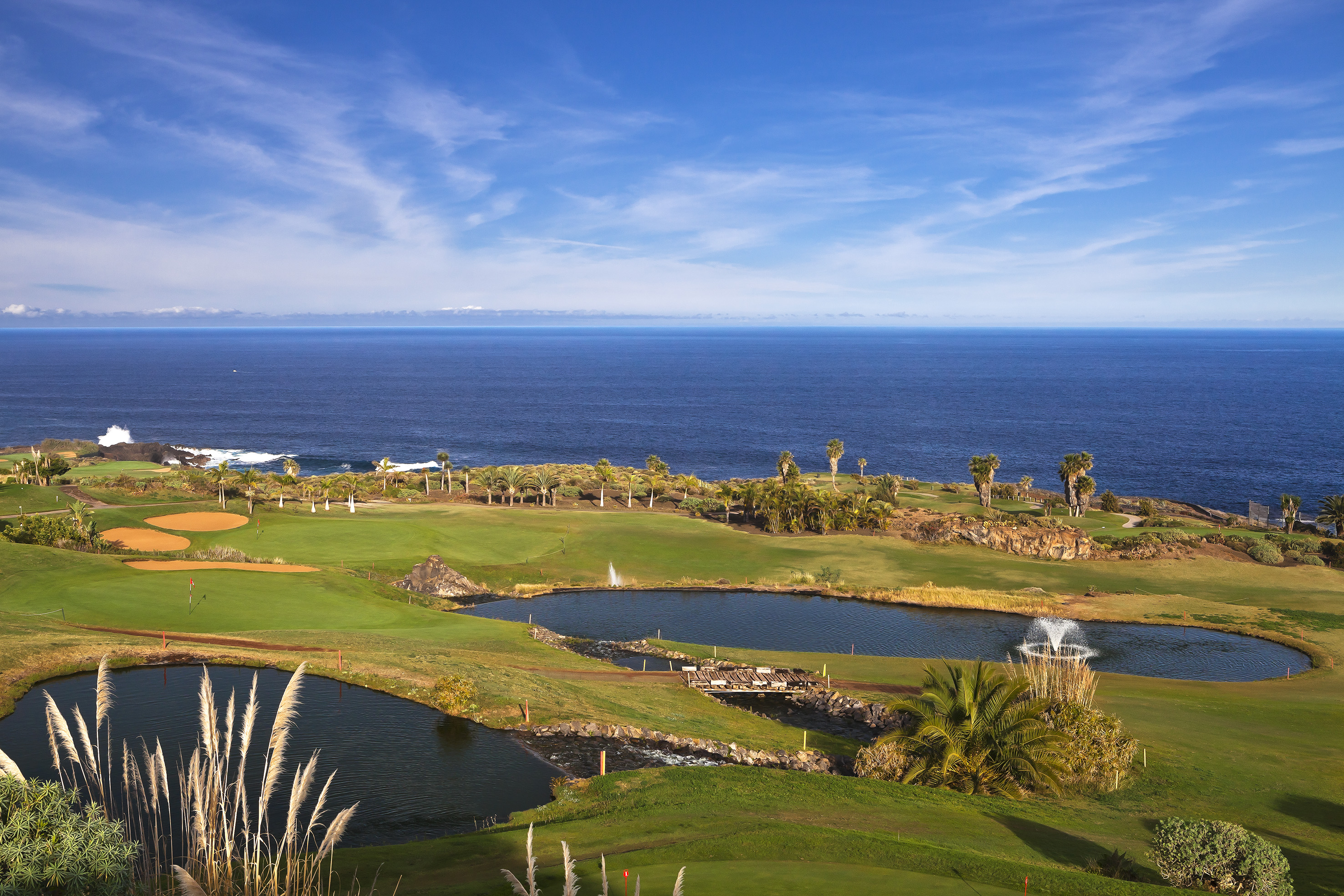 Ocean view golf course with green fairways, lakes, fountains, and palm trees.