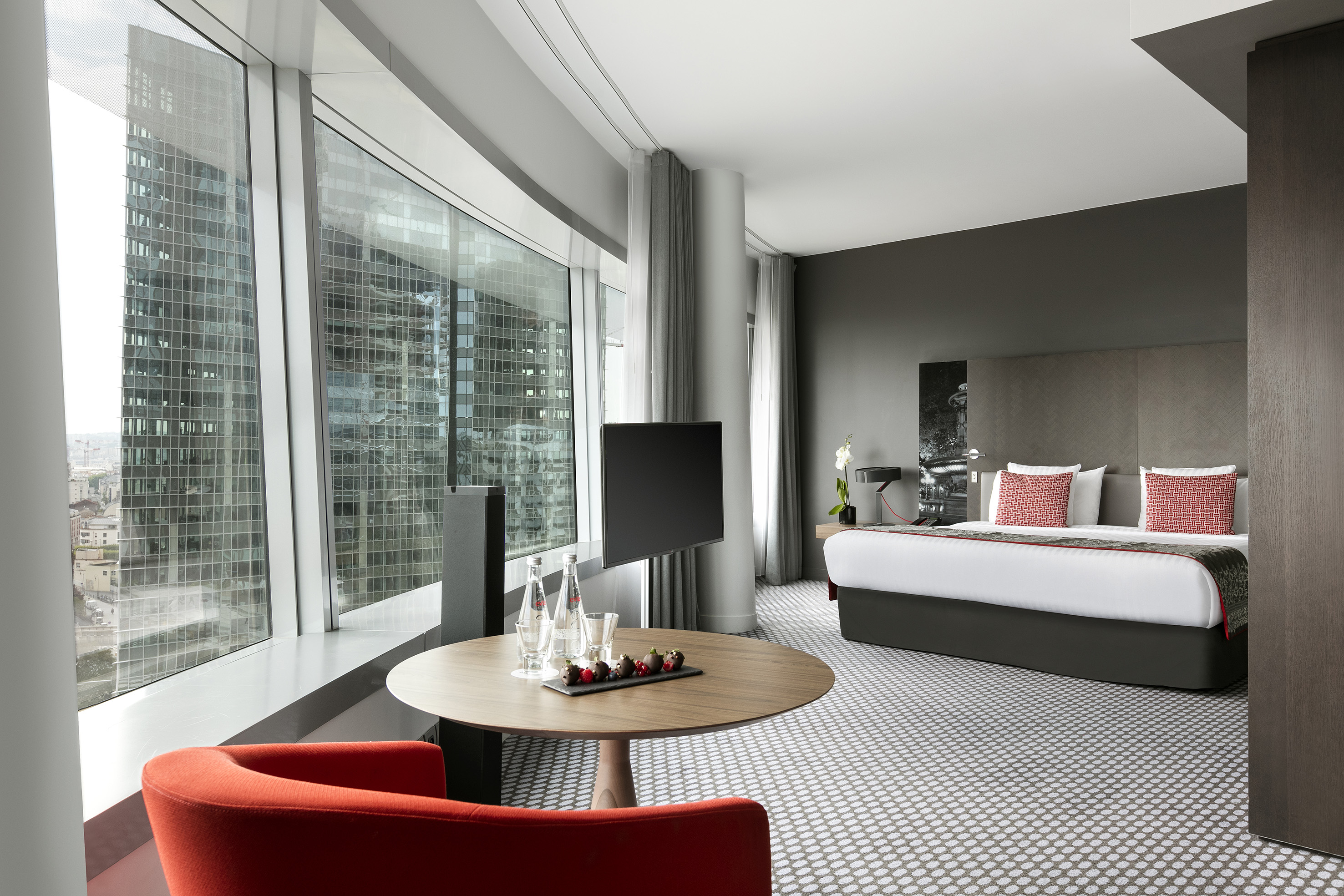 Modern hotel suite with panoramic city view, bed, and stylish seating.