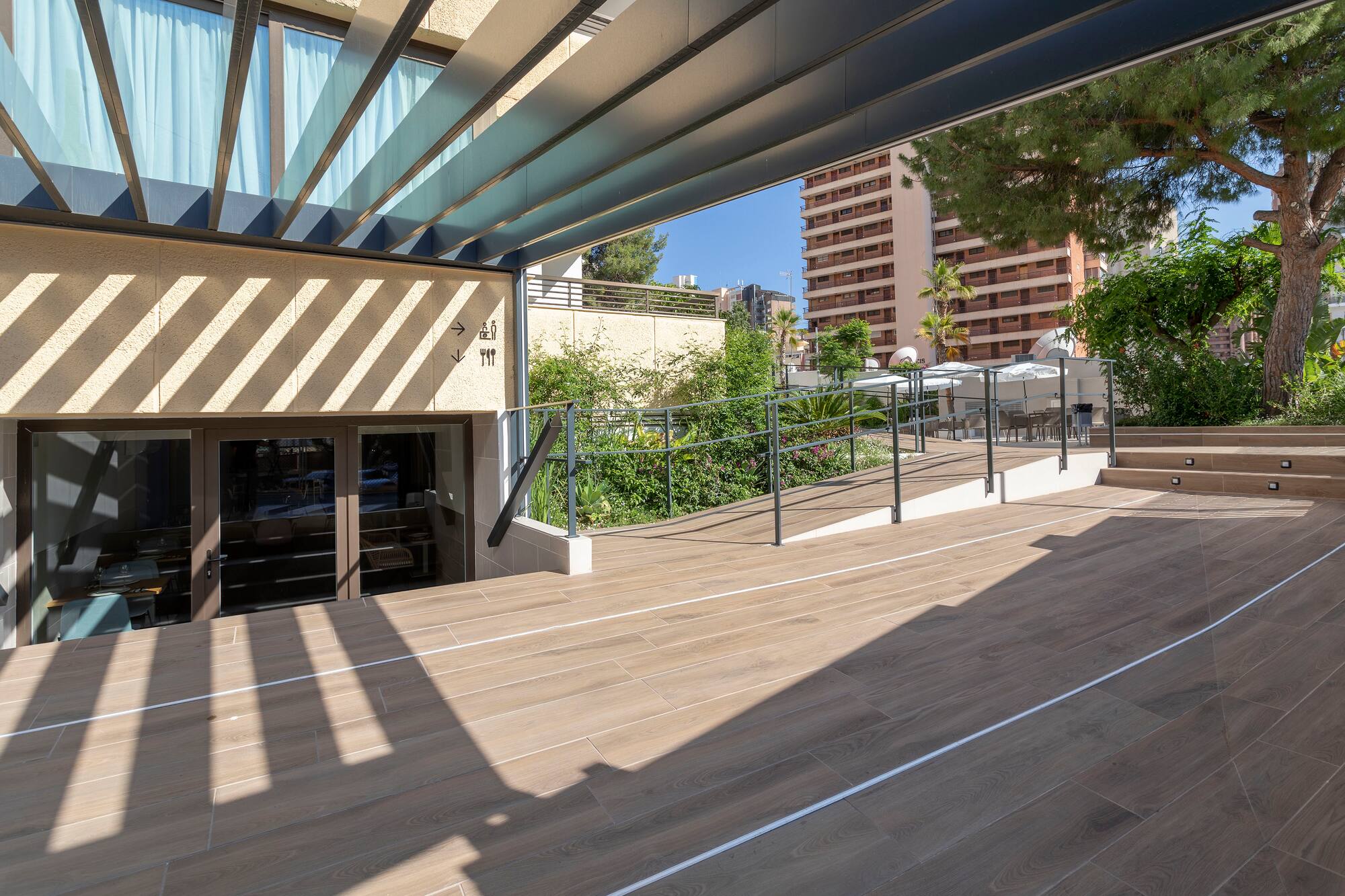 Modern hotel patio with wood-look floor, slatted canopy, accessibility ramp.