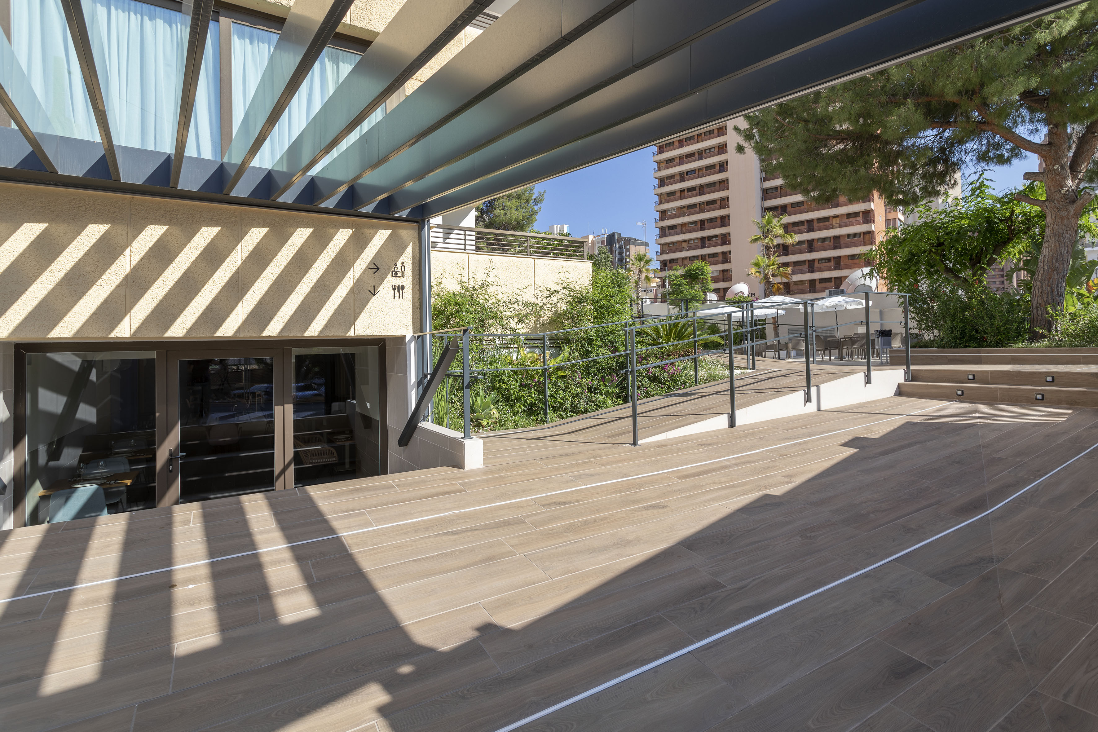 Modern hotel patio with wood-look floor, slatted canopy, accessibility ramp.
