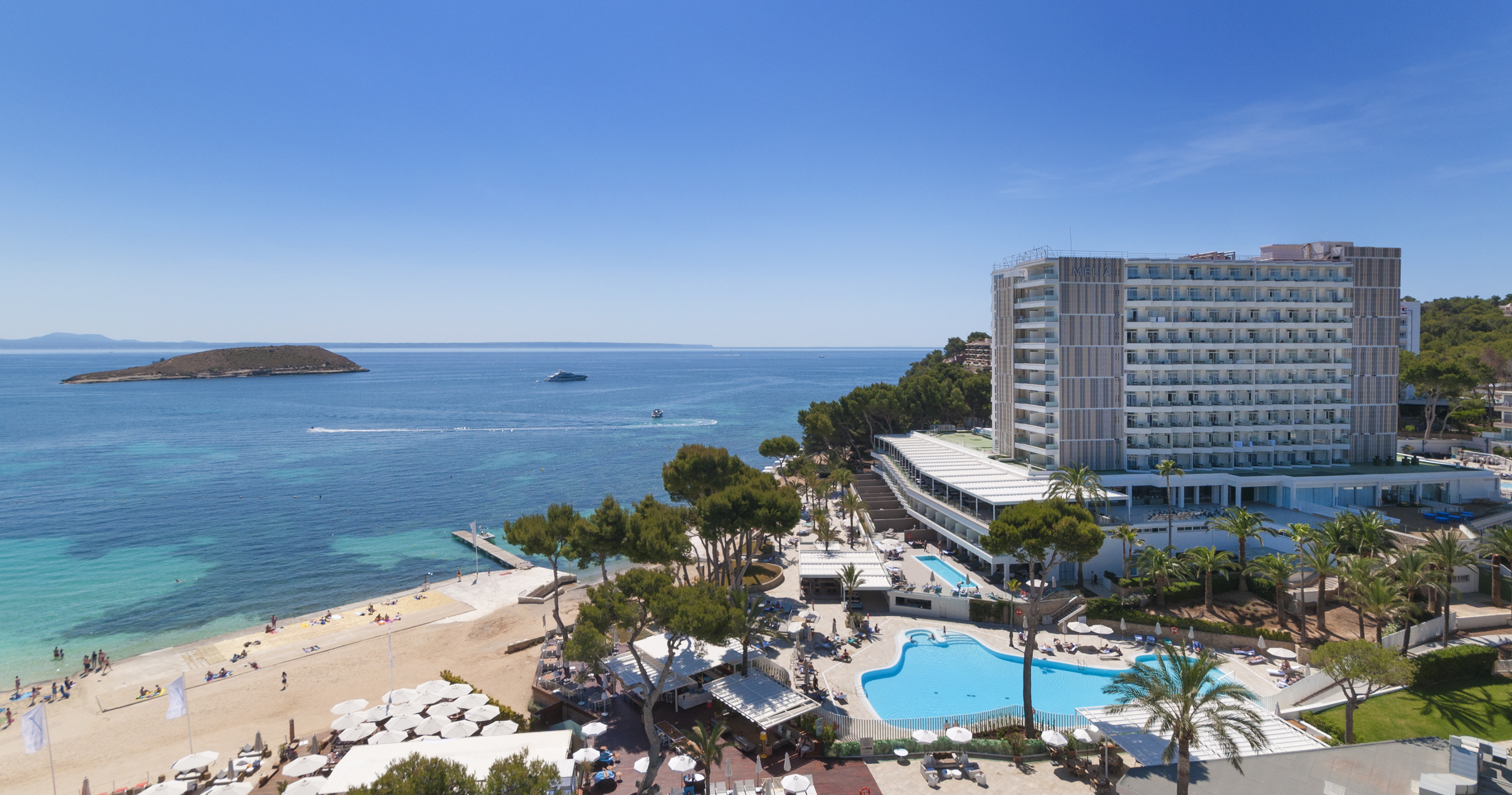 Aerial view Melia beach resort with pools, sandy shore, ocean, and distant island.
