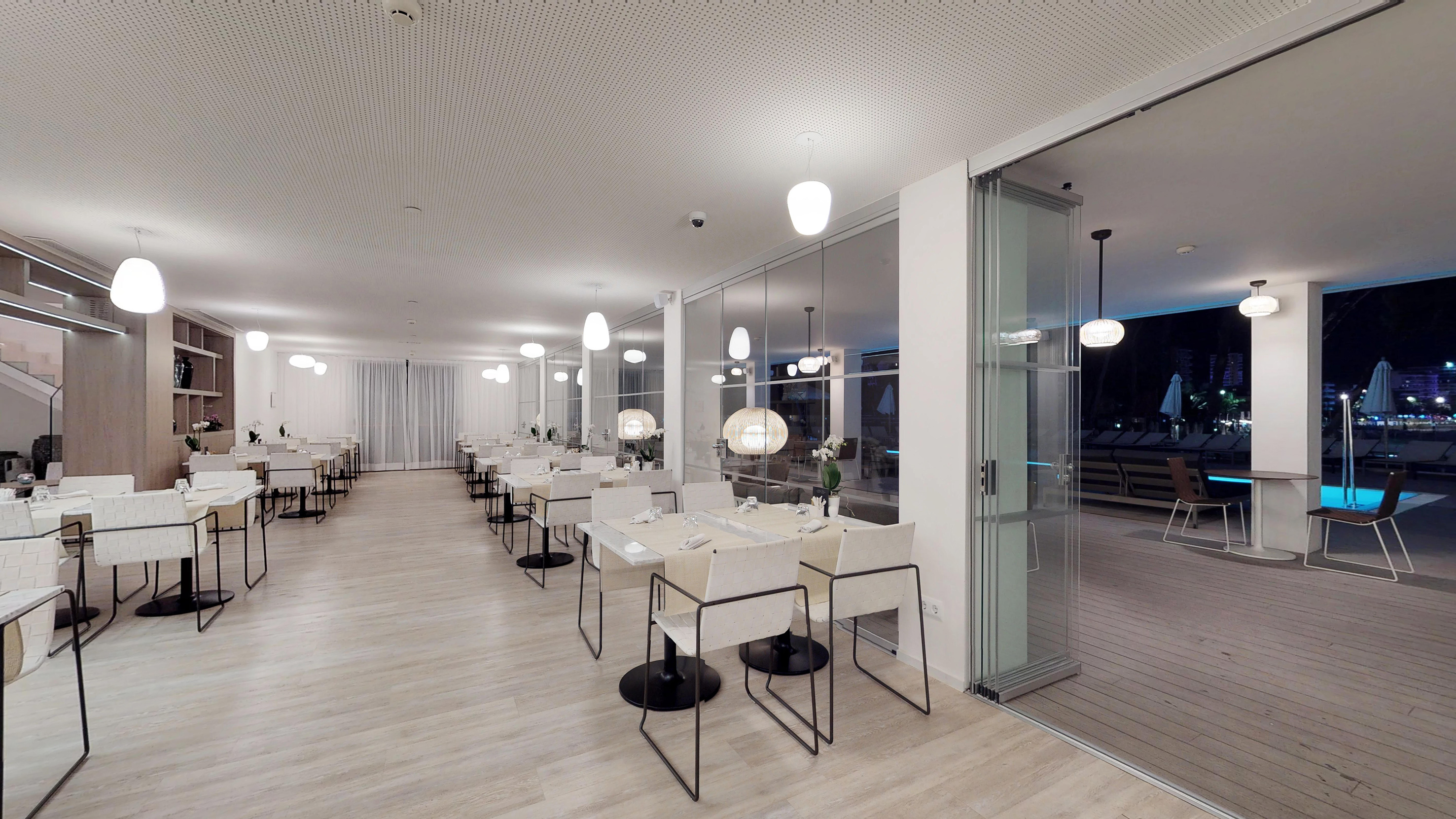 Elegant modern restaurant with white tables and poolside view at night.